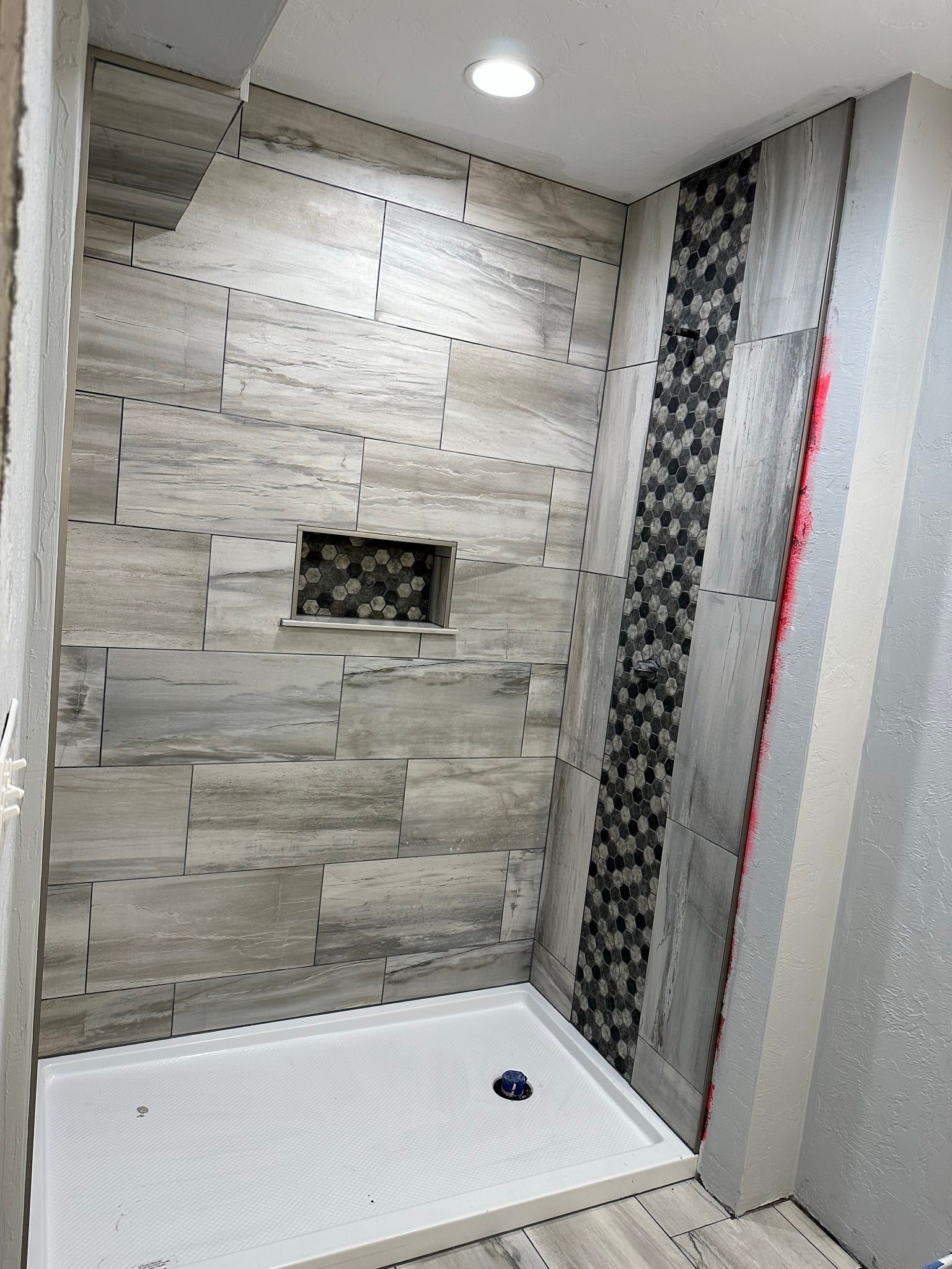 Shower with light gray stone-like tile and a mosaic accent strip. A built-in niche and white shower pan.