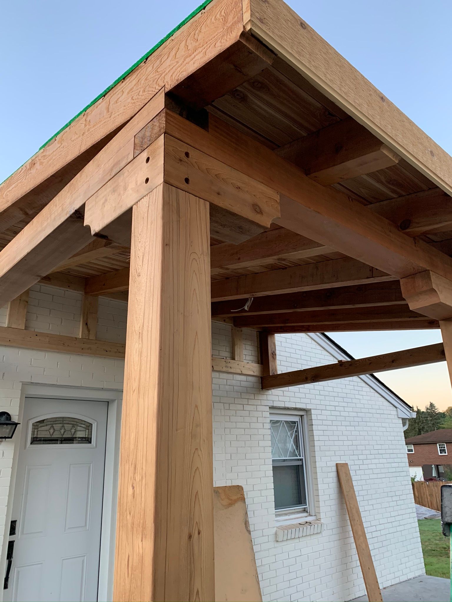 Wooden porch under construction on a white brick house, with visible beams and supports.