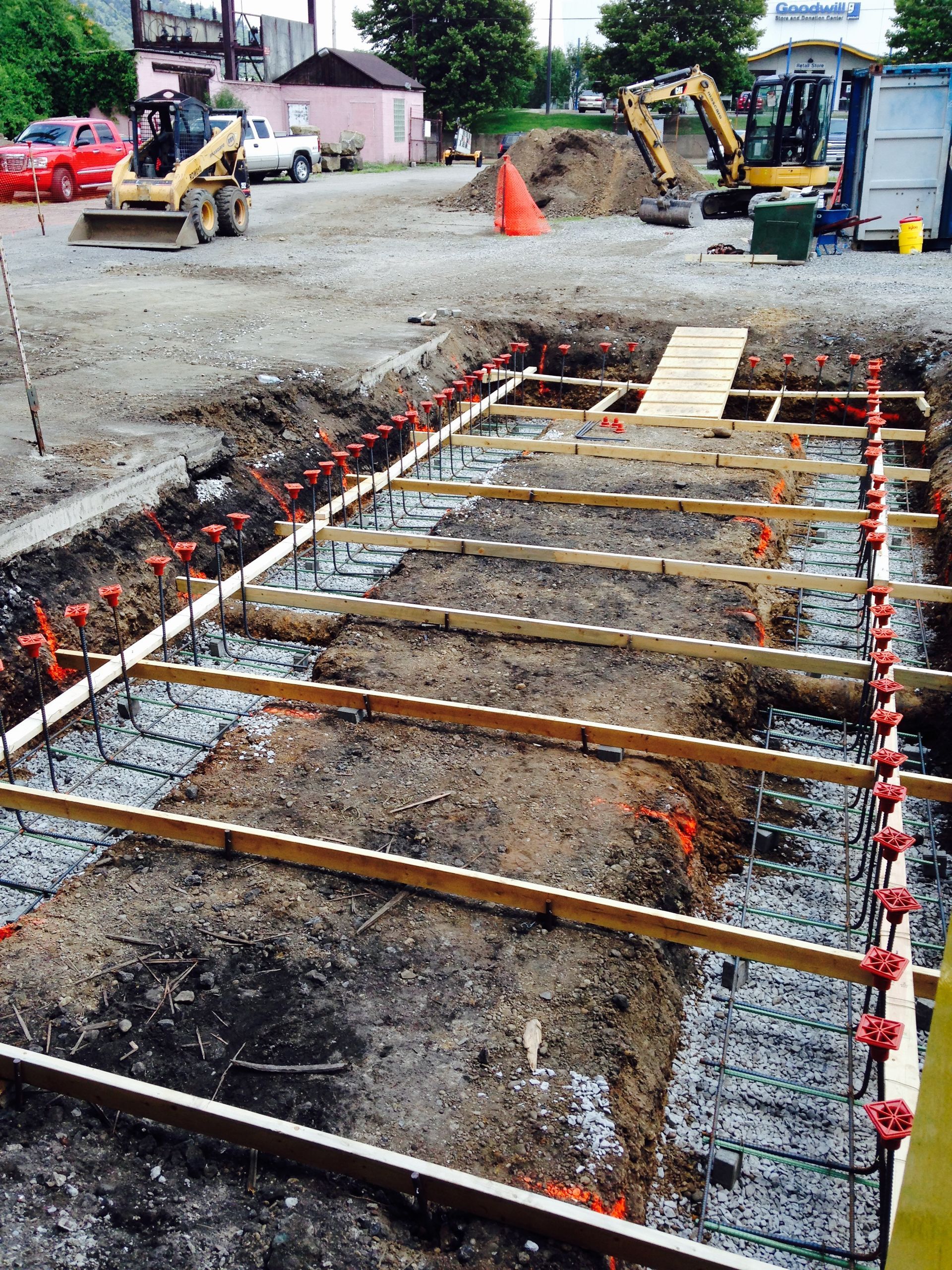 Construction site with excavated foundation, rebar, wood forms, and heavy equipment.
