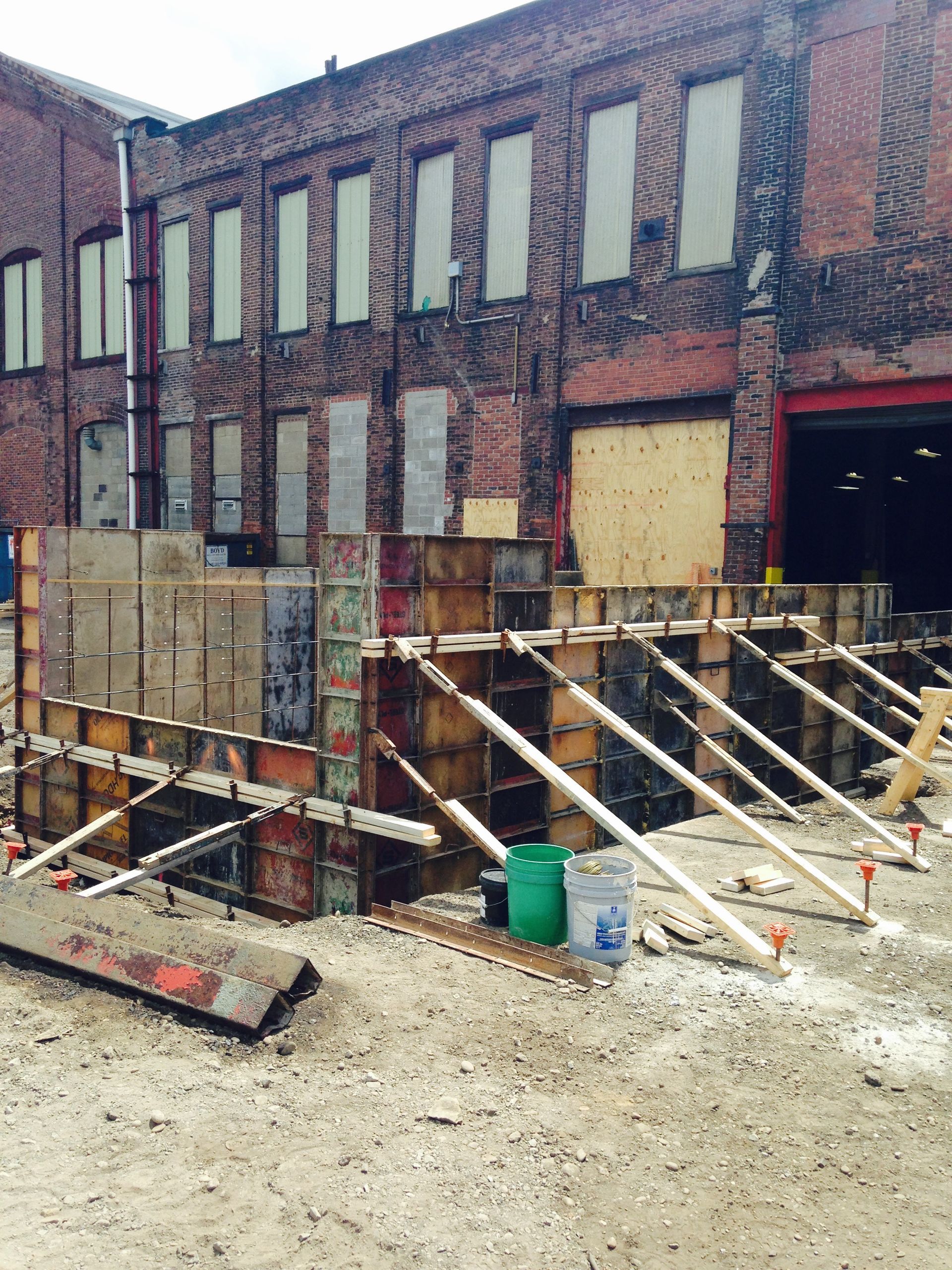 Construction site: wooden forms for a concrete structure in front of a brick building.