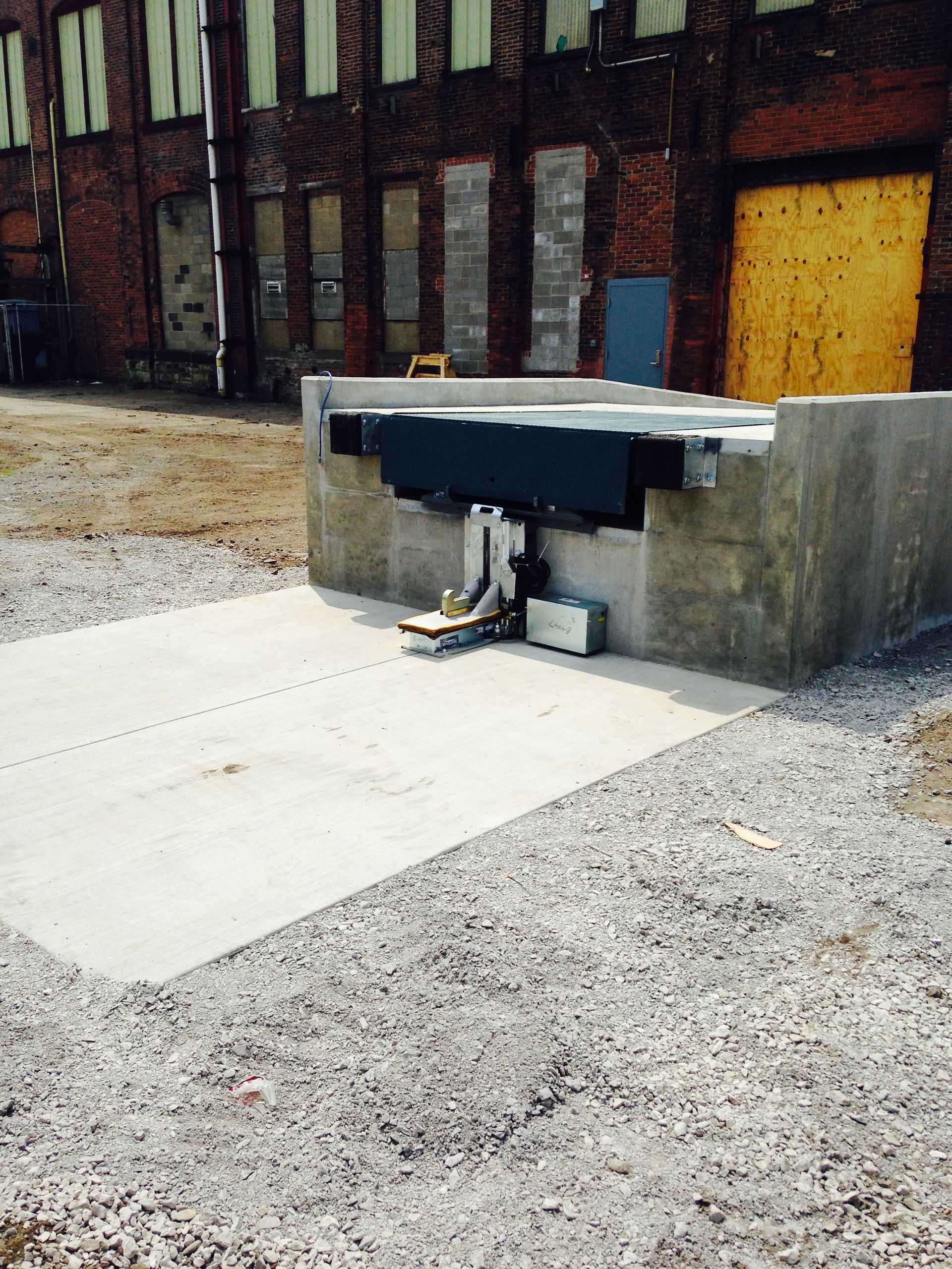 Concrete loading dock with gravel surround in front of a brick building.