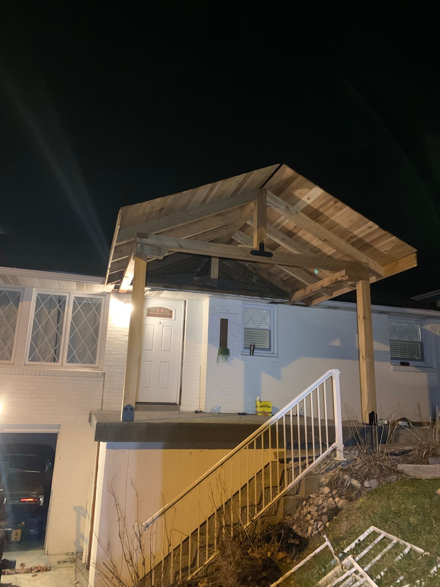 Exterior of a white building at night, with a wooden awning over a door and a staircase with a white railing.