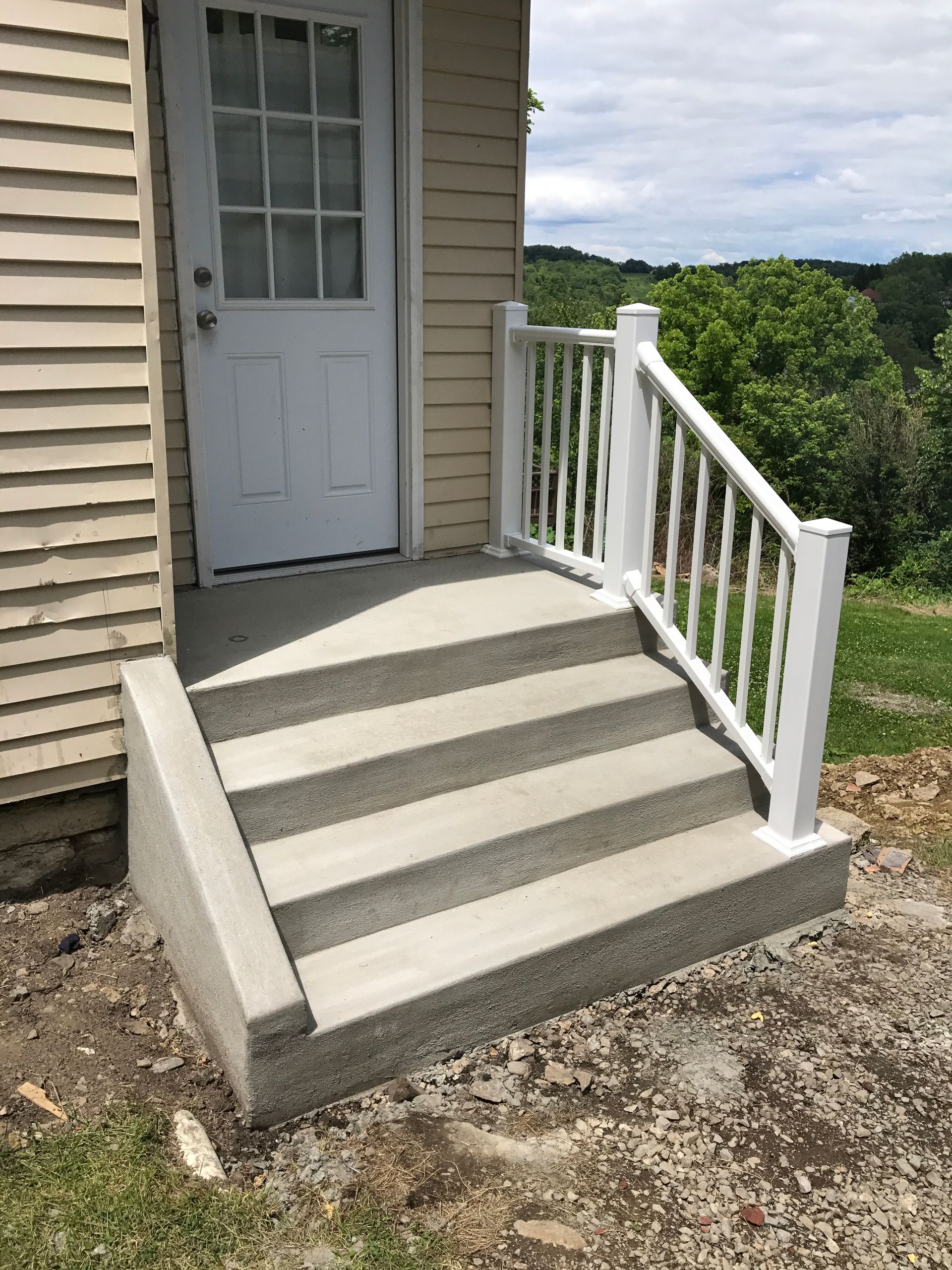 Concrete steps with a white railing leading up to a white door on the side of a building.