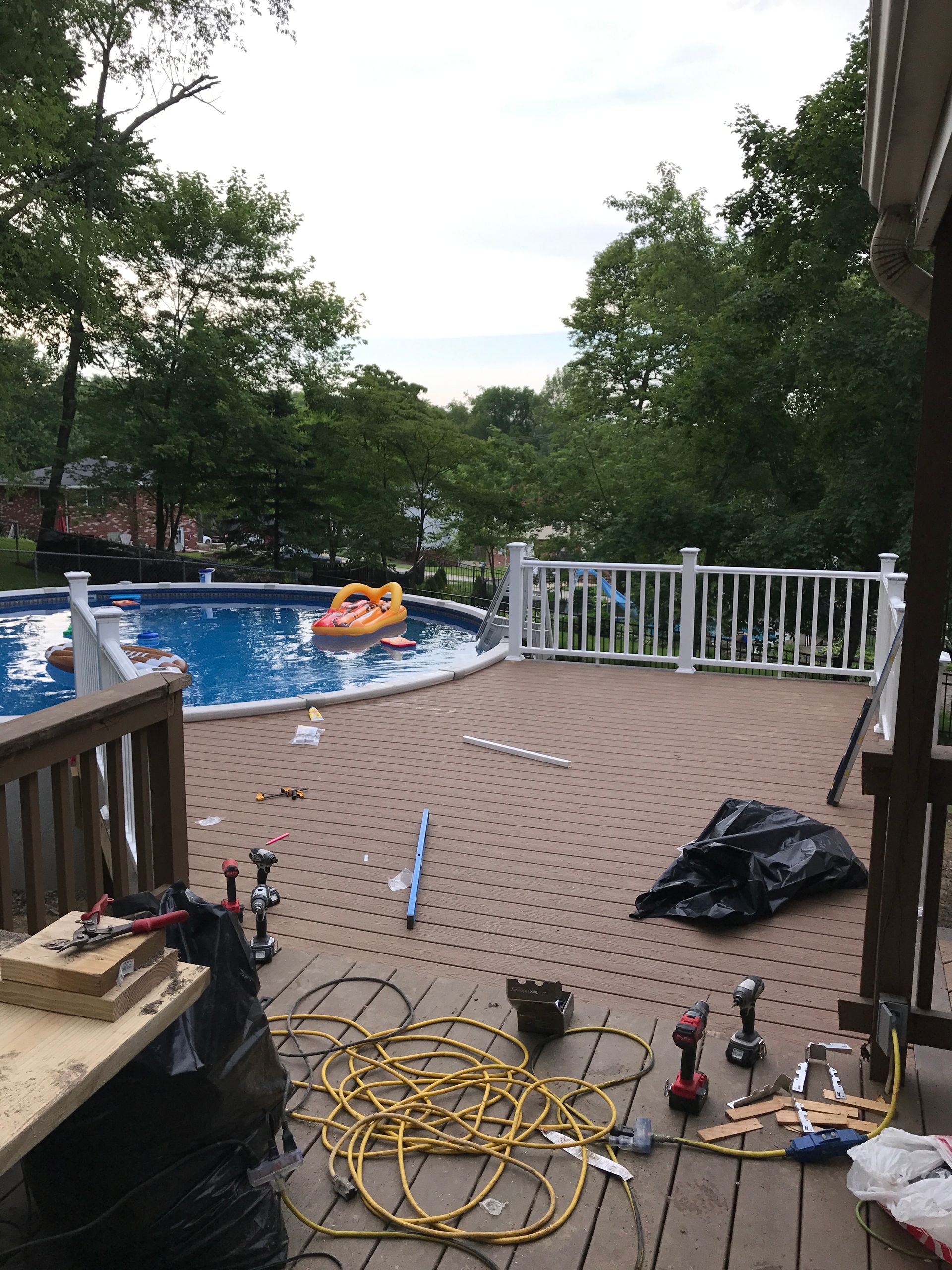 Deck under construction with pool in the background. Tools, yellow cable, and black trash bag scattered about.