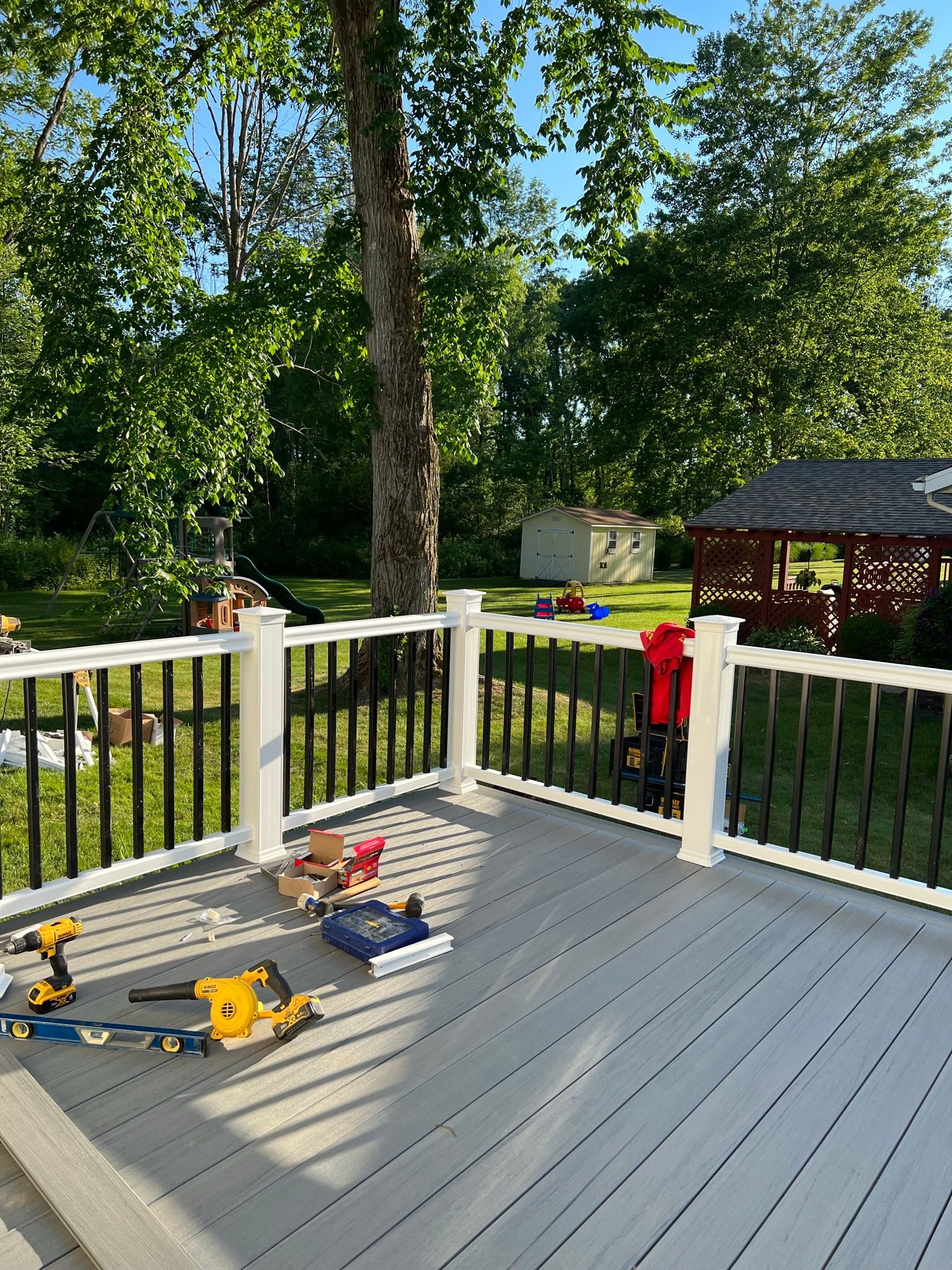 Deck with tools in the foreground, yard and trees in the background. Sunny, daylight setting.