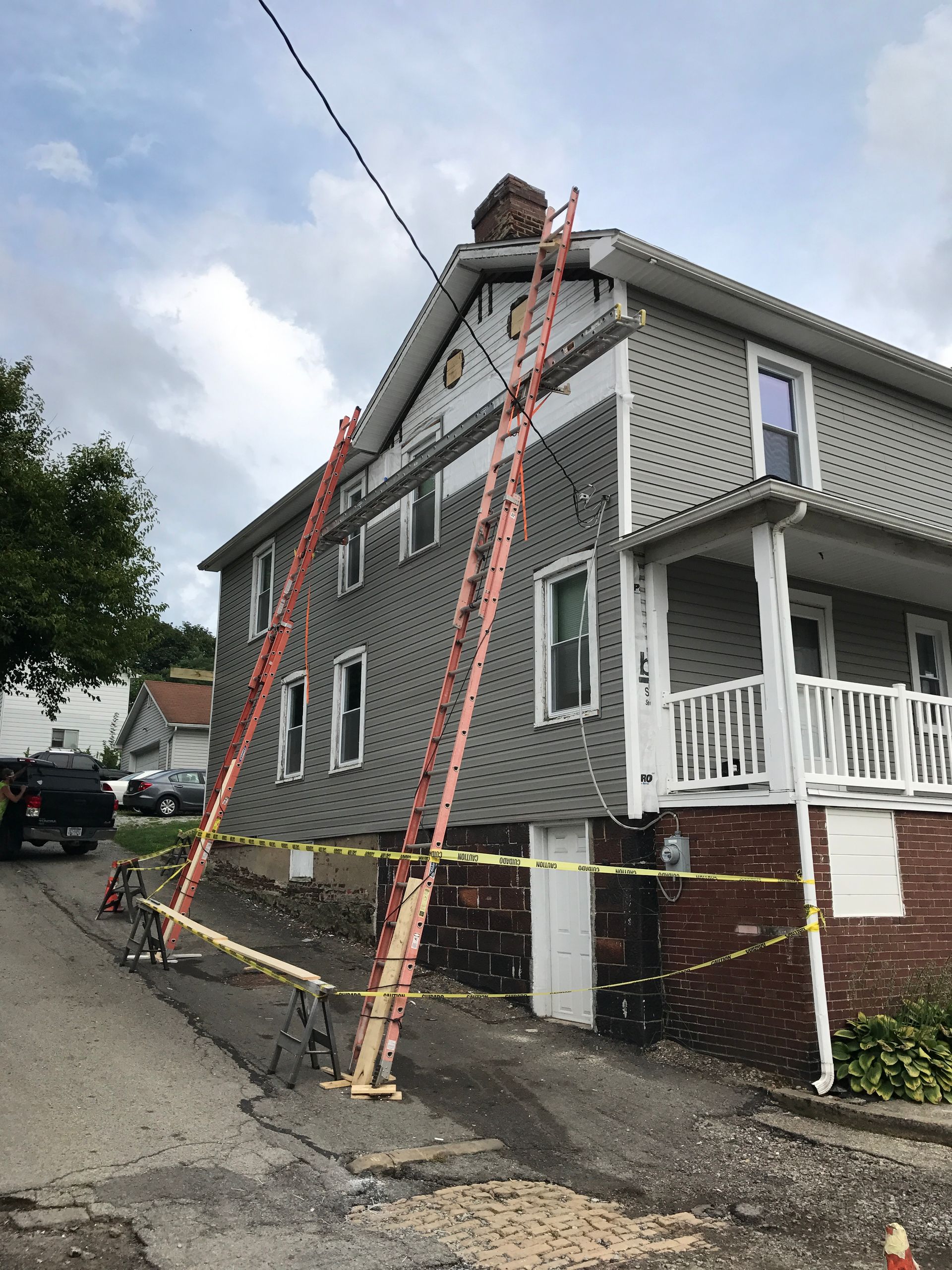 Two tall ladders propped against a two-story house; yellow tape surrounds the building on the street.