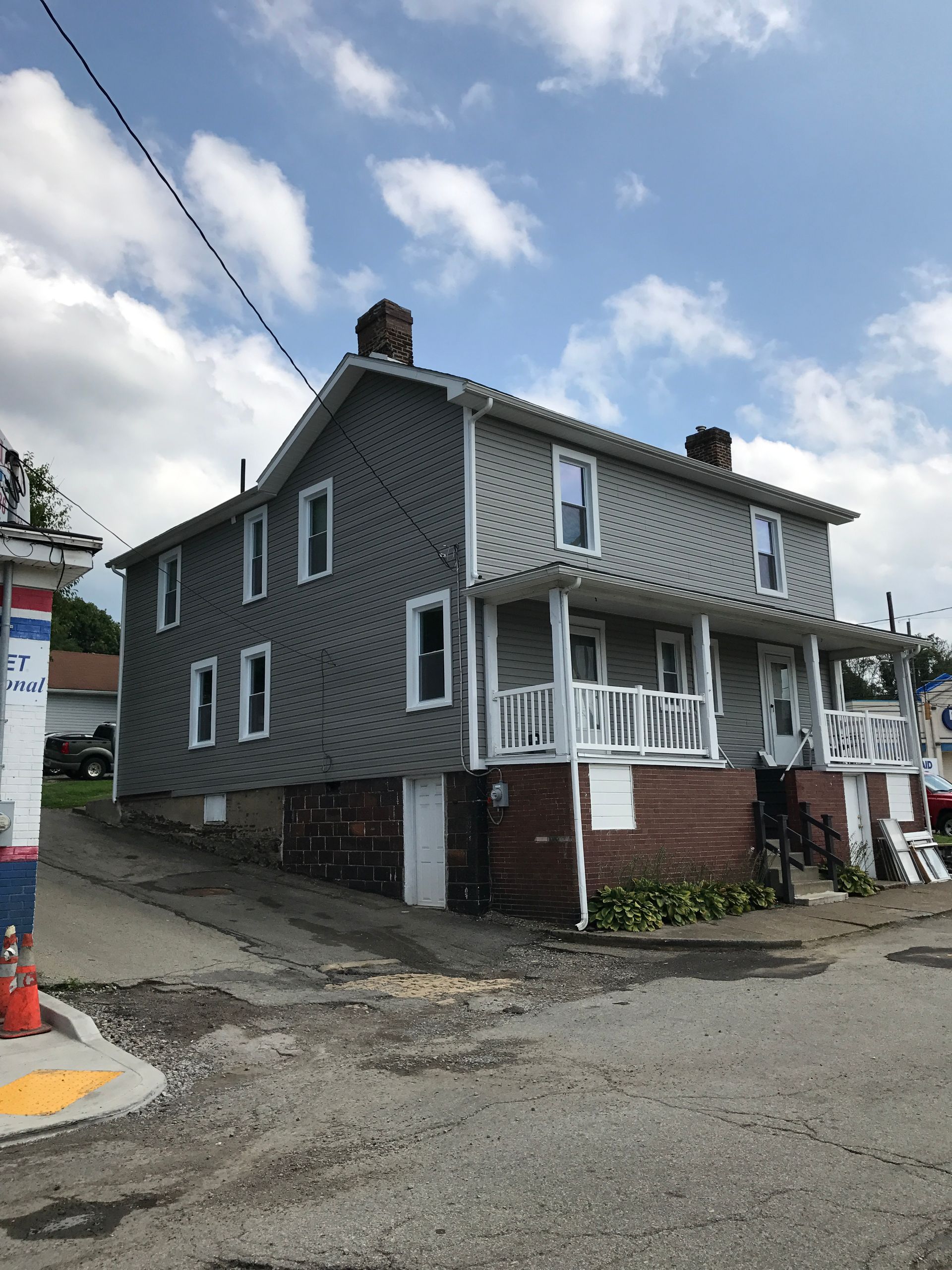 Two-story gray house with white trim, brick foundation, and a small porch on a corner lot.