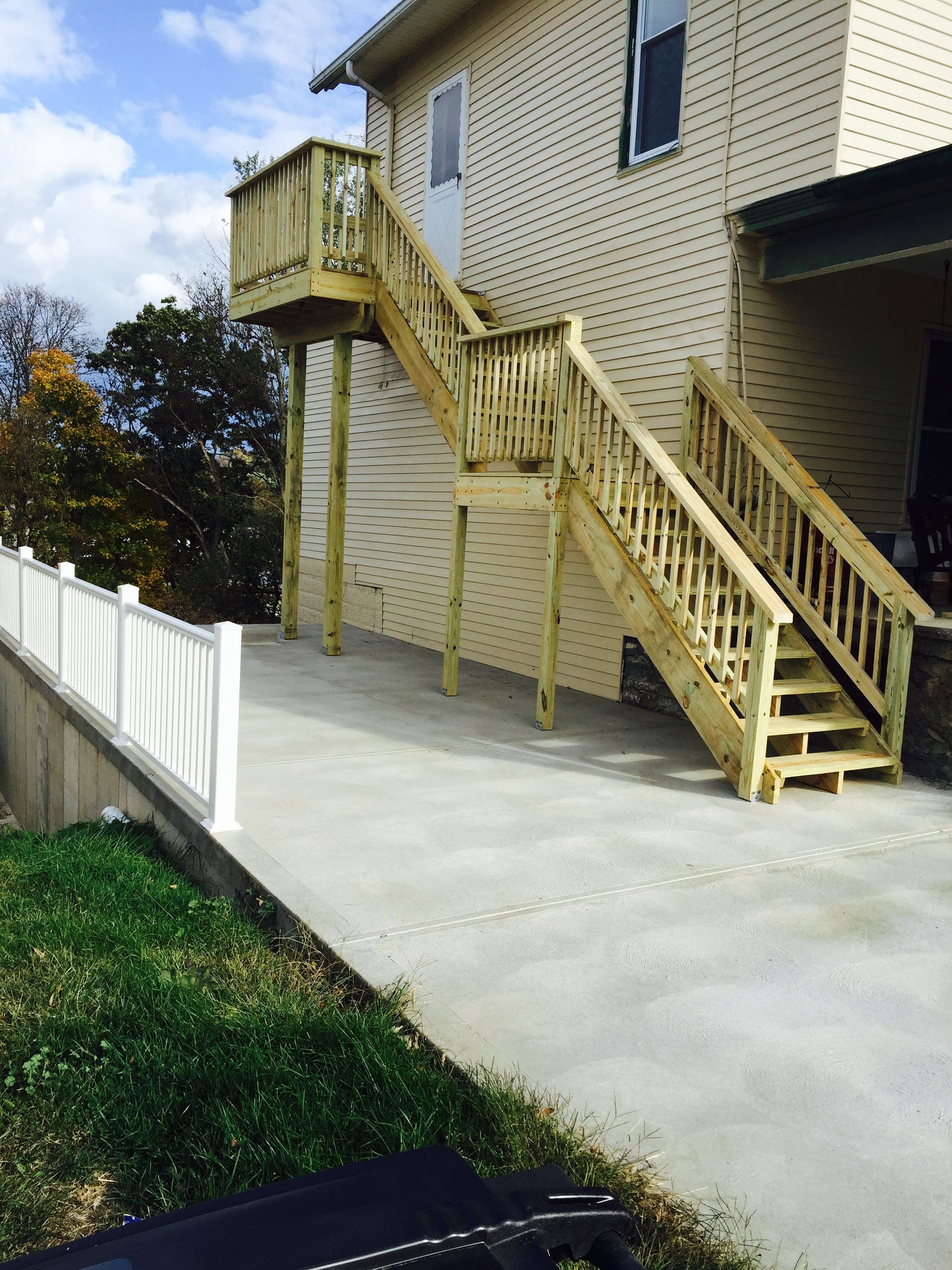 Wooden exterior staircase to a second-story door, descending to a concrete patio. Light-colored siding and railing.