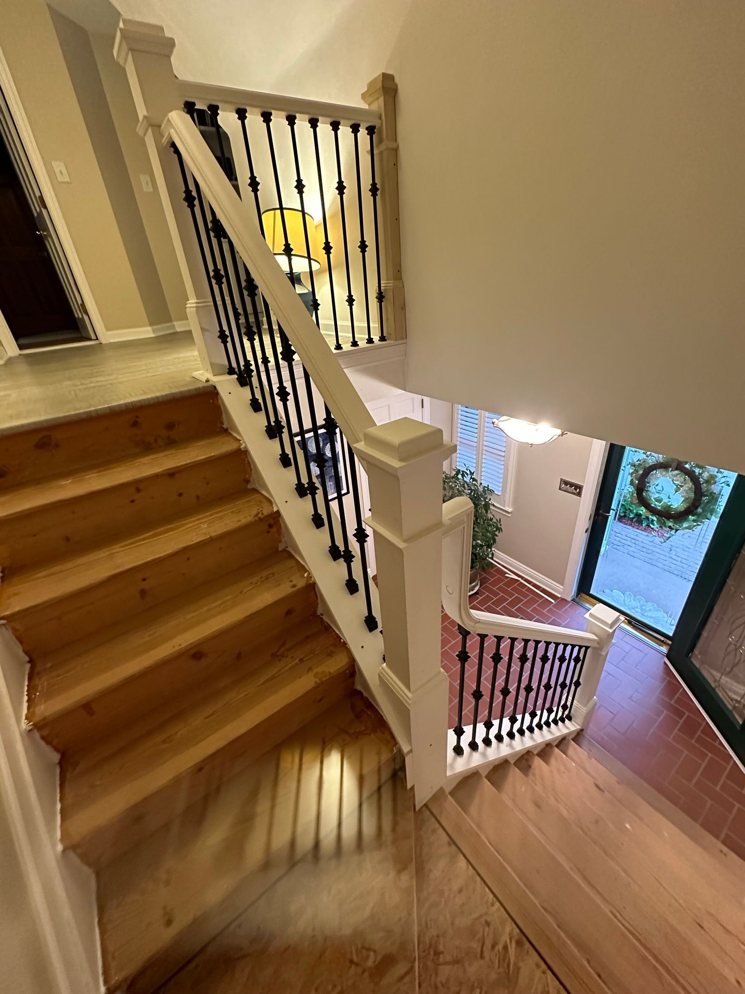Staircase with wooden steps, white railing, and black spindles. The entry door is visible.