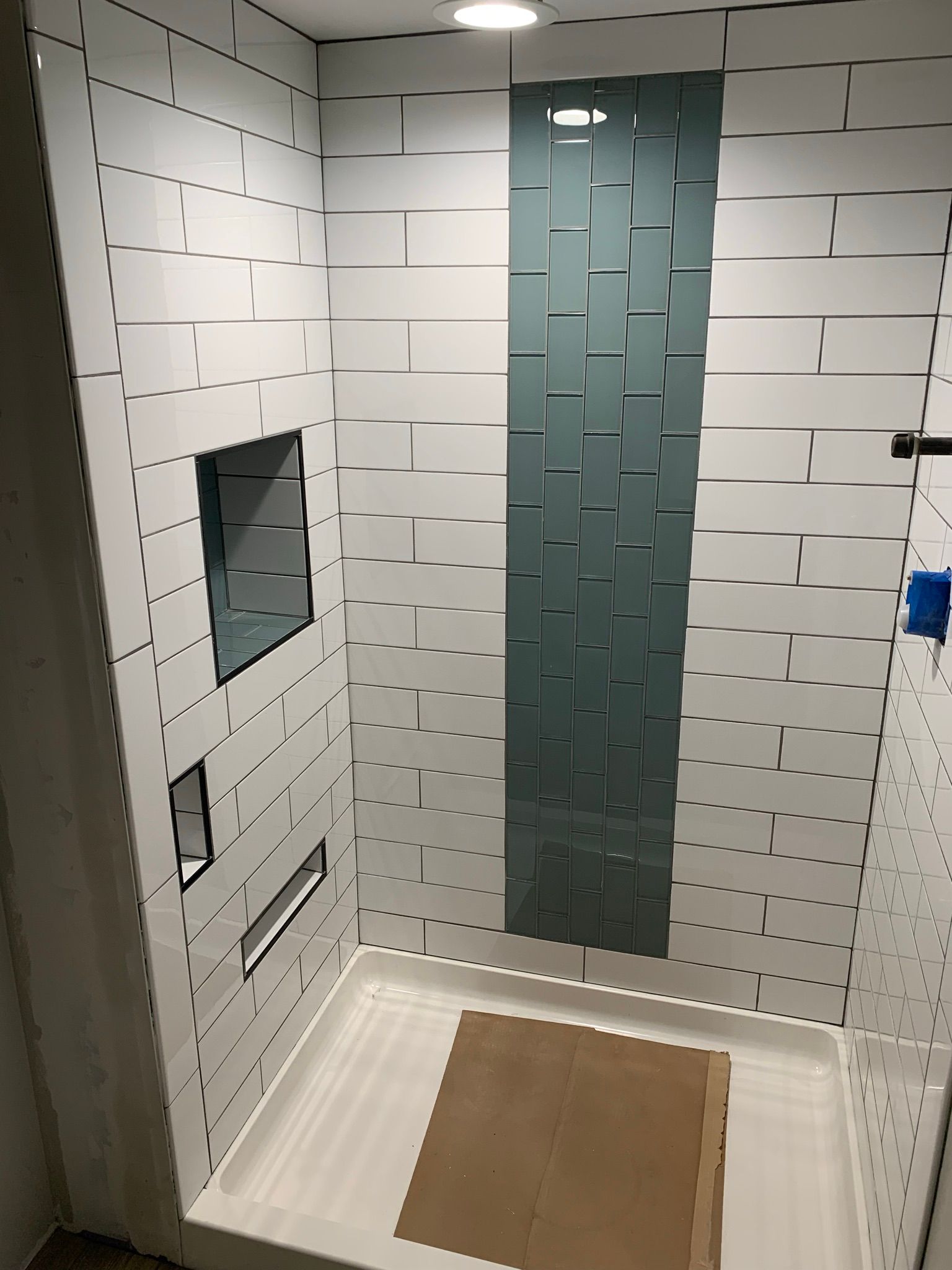 White tiled shower with blue accent strip and recessed shelves.