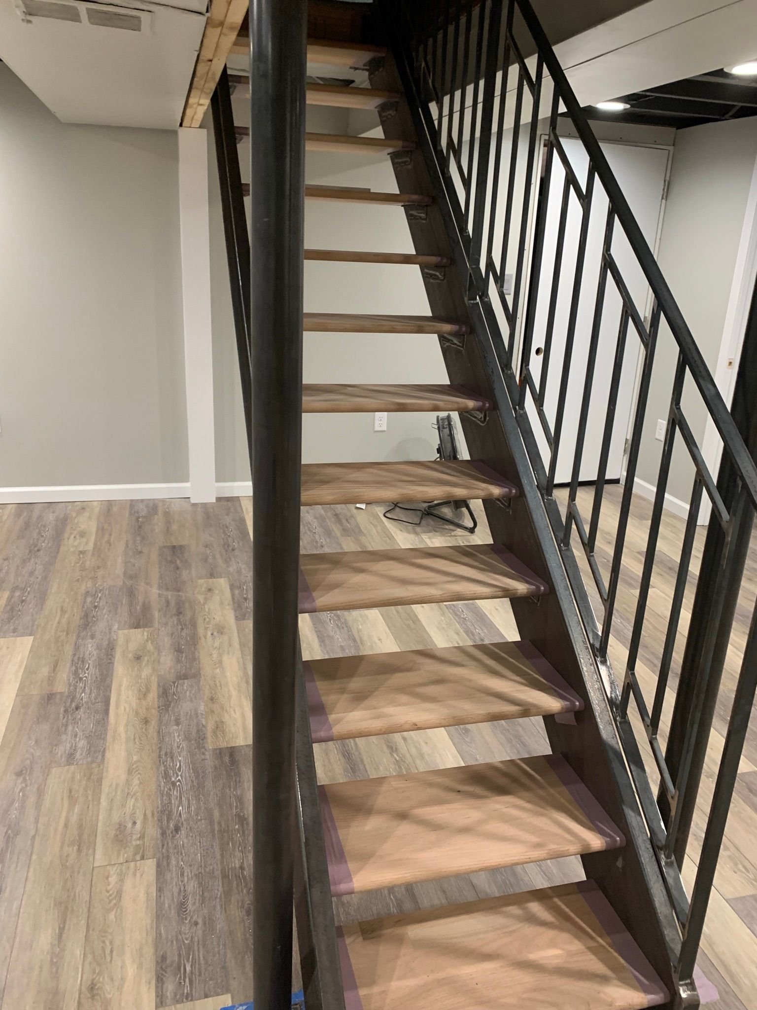 Wooden spiral staircase with black metal railing and central column, in a room with wood-look flooring.