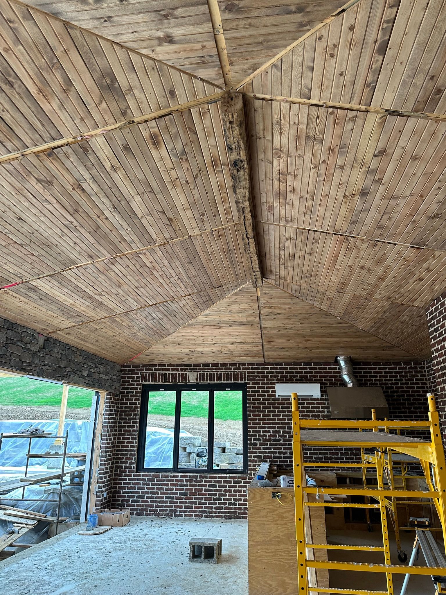 Interior view of a building under construction, showing the wooden ceiling and brick walls. Scaffolding present.