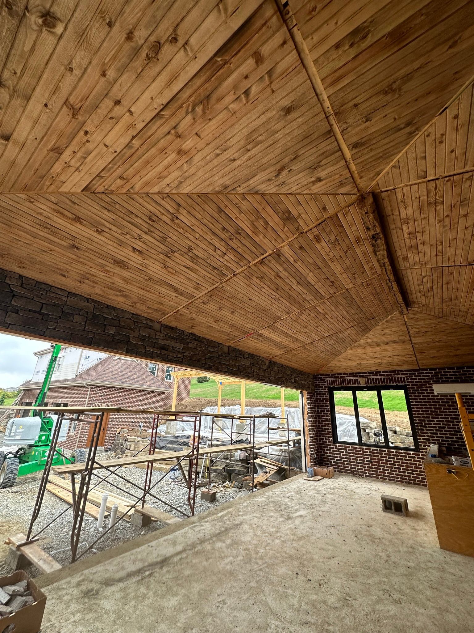 Wooden ceiling of a building under construction, overlooking a work site and outdoor area.
