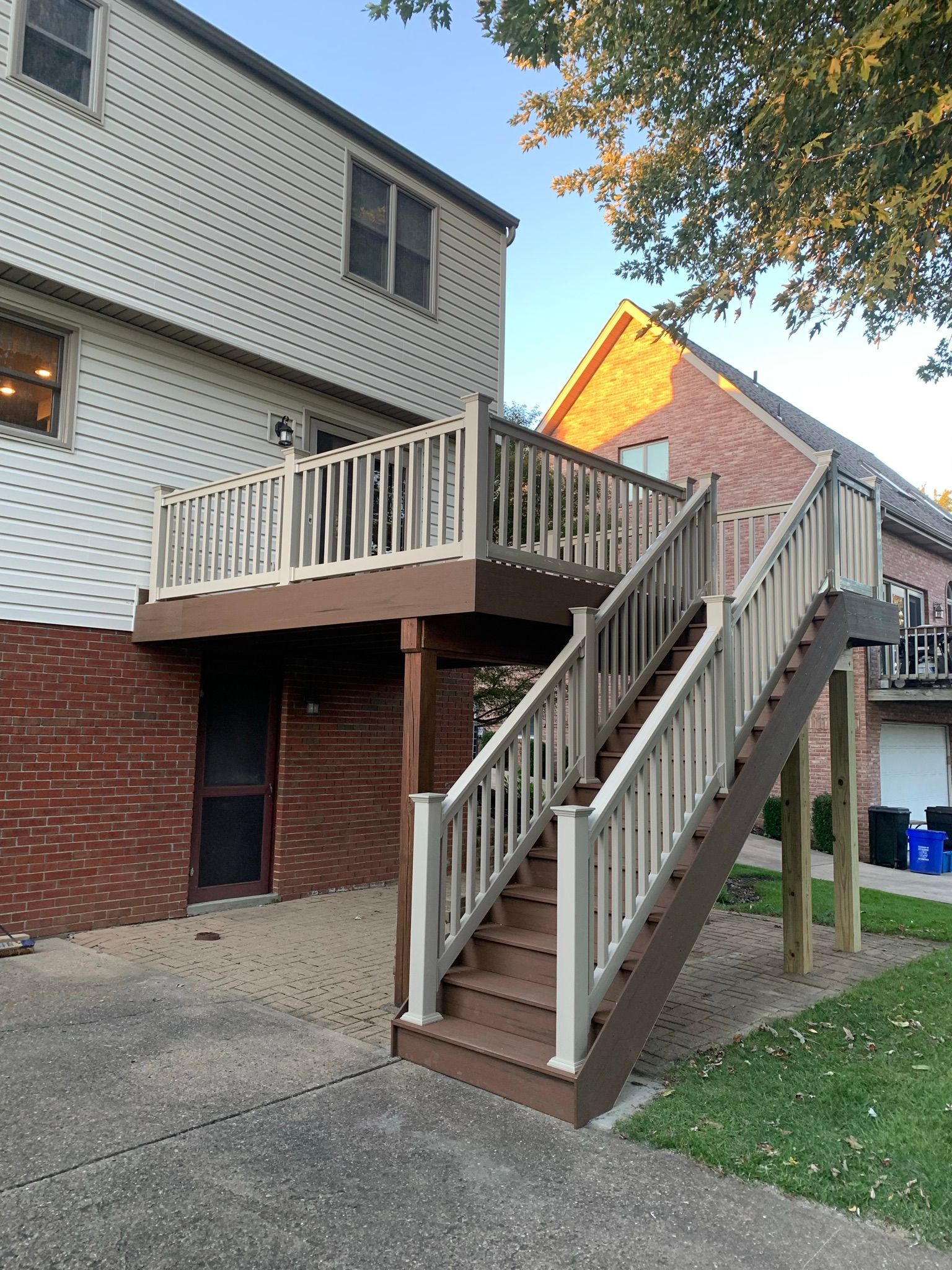 Two-story deck with stairs, tan and brown, attached to brick and siding building.