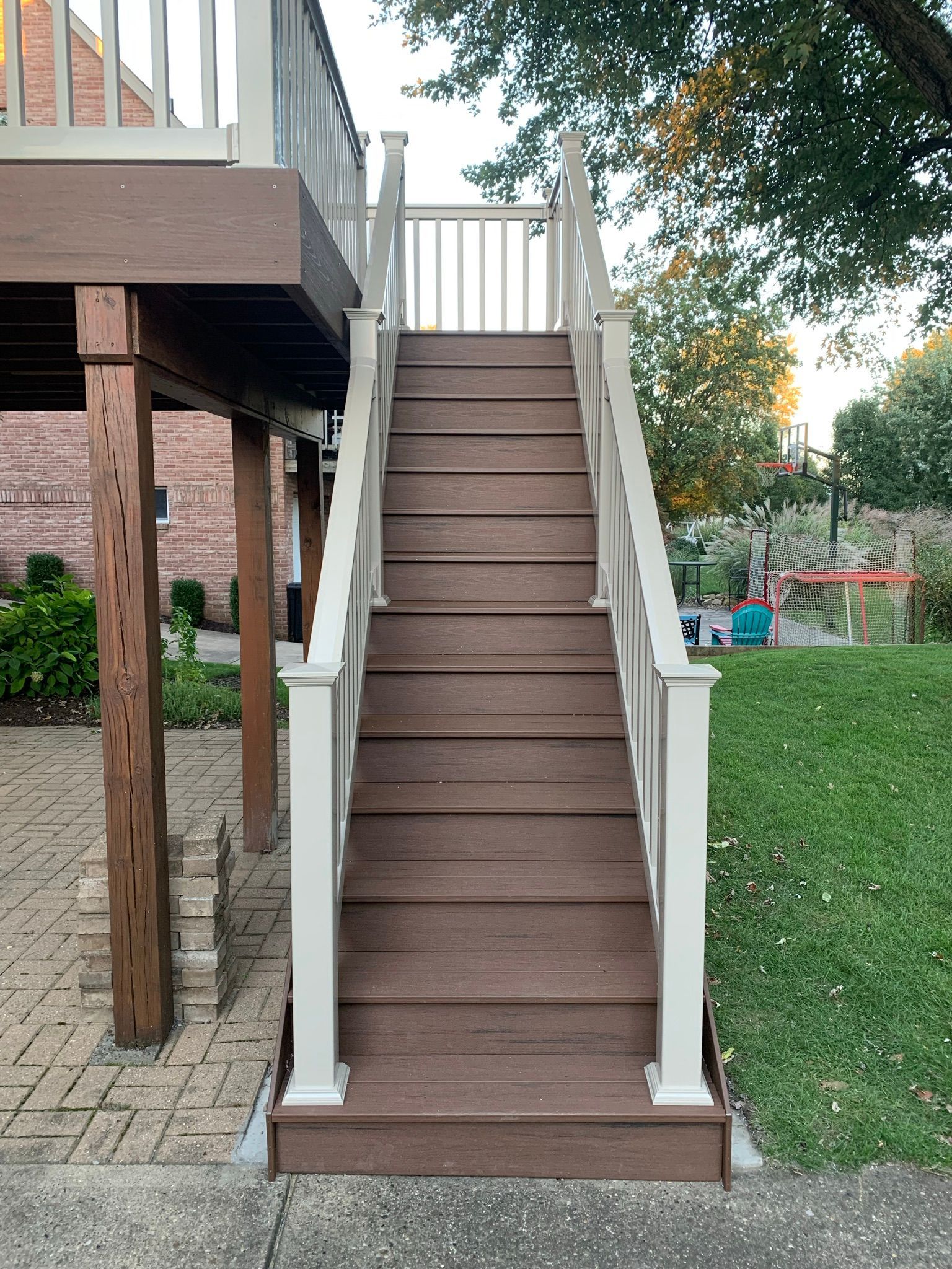 Wooden stairs leading up to a deck with white railings, set in a backyard.