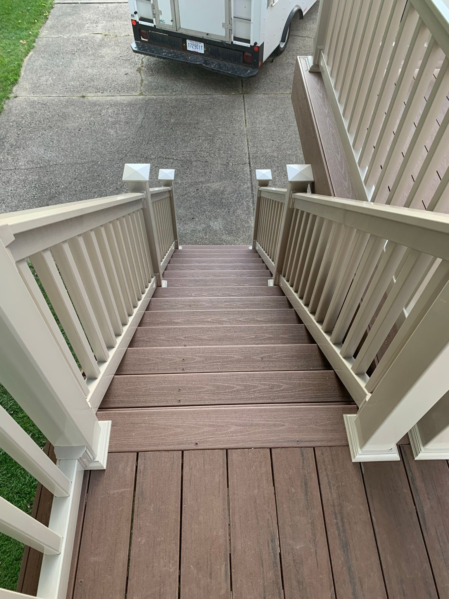 Staircase with tan railing and brown steps leading down to a driveway.