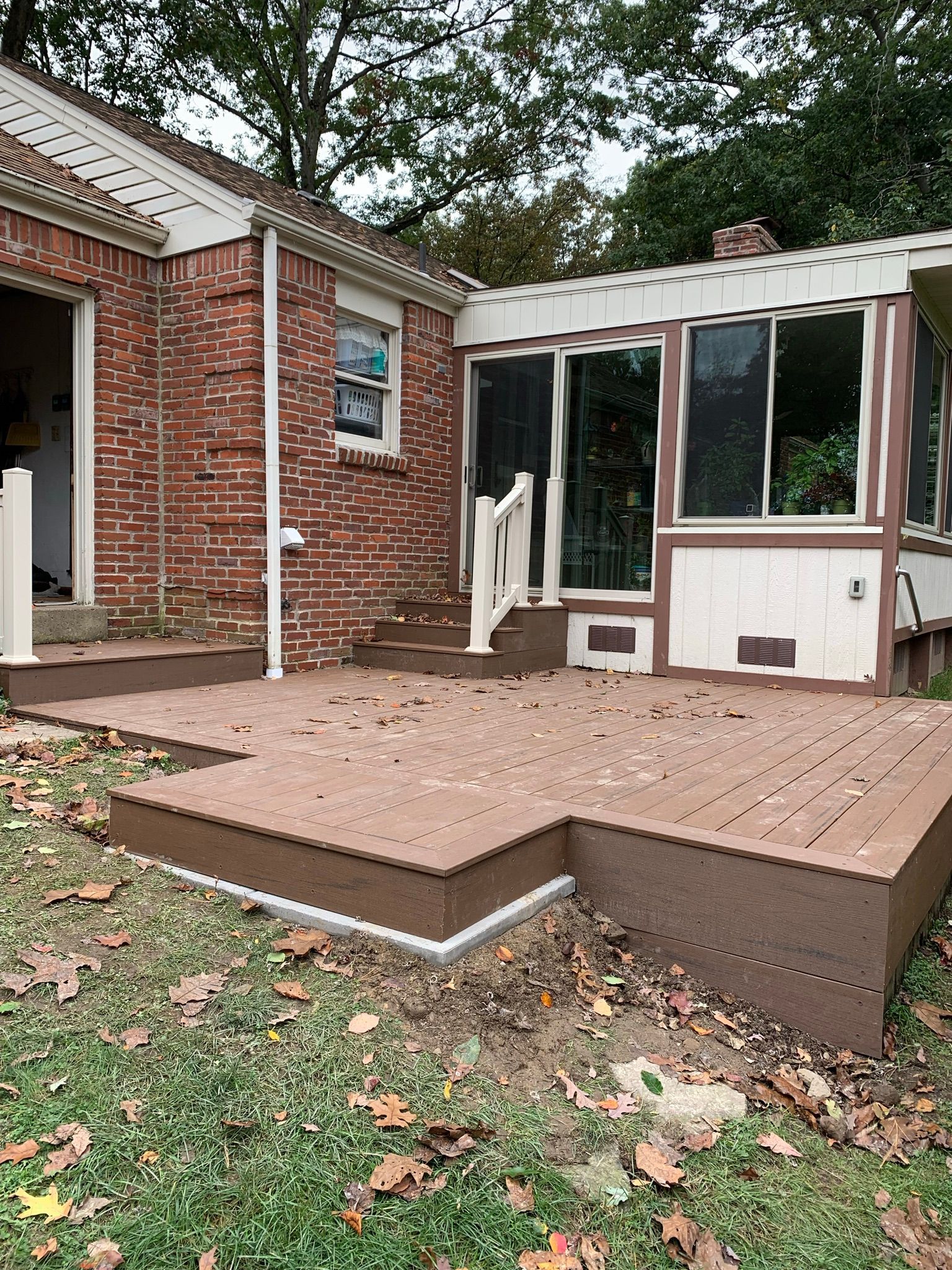Brown composite deck with brick house and sunroom in background.