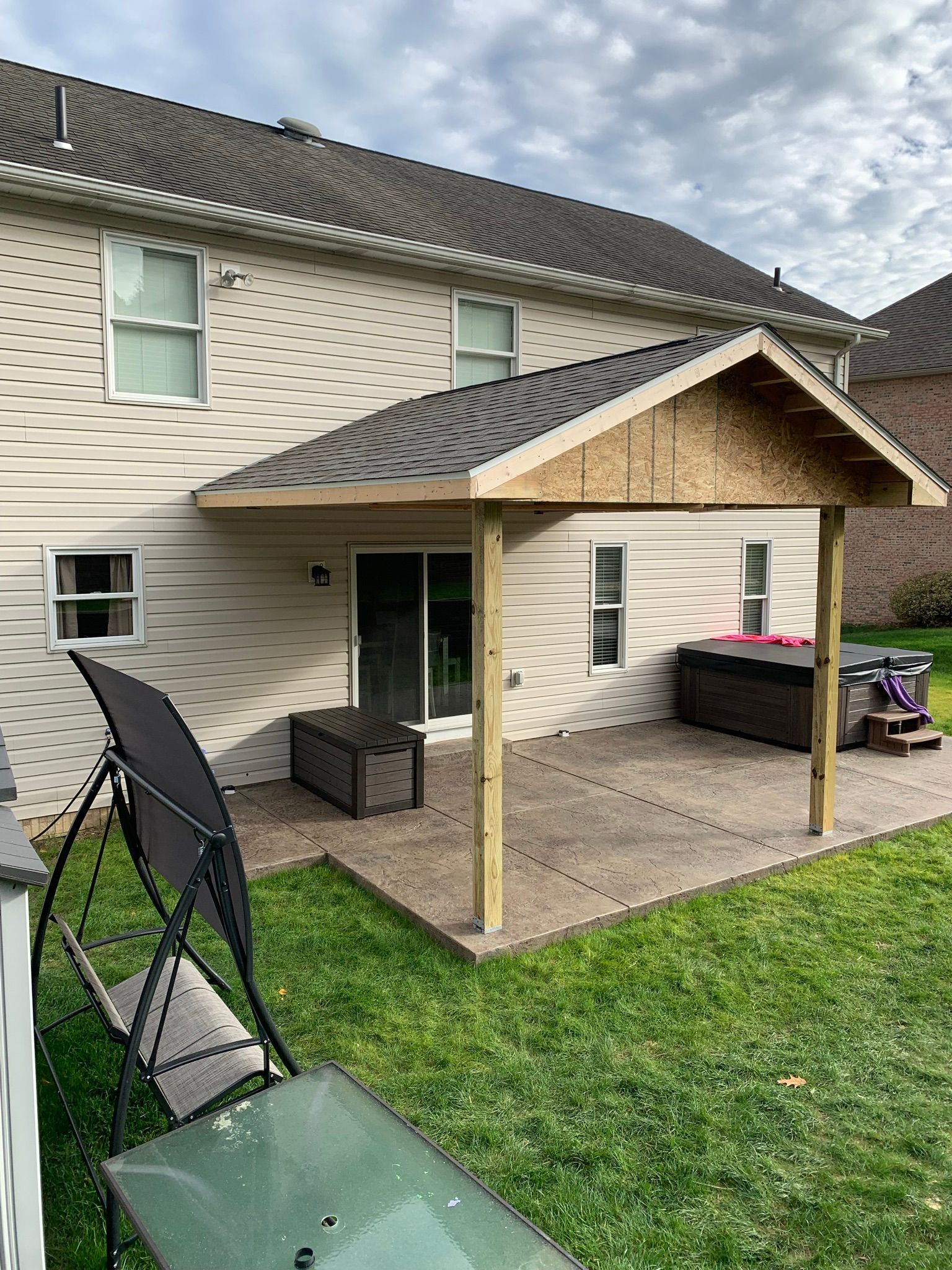 Backyard patio with a newly constructed roof, hot tub, and yard with grass.