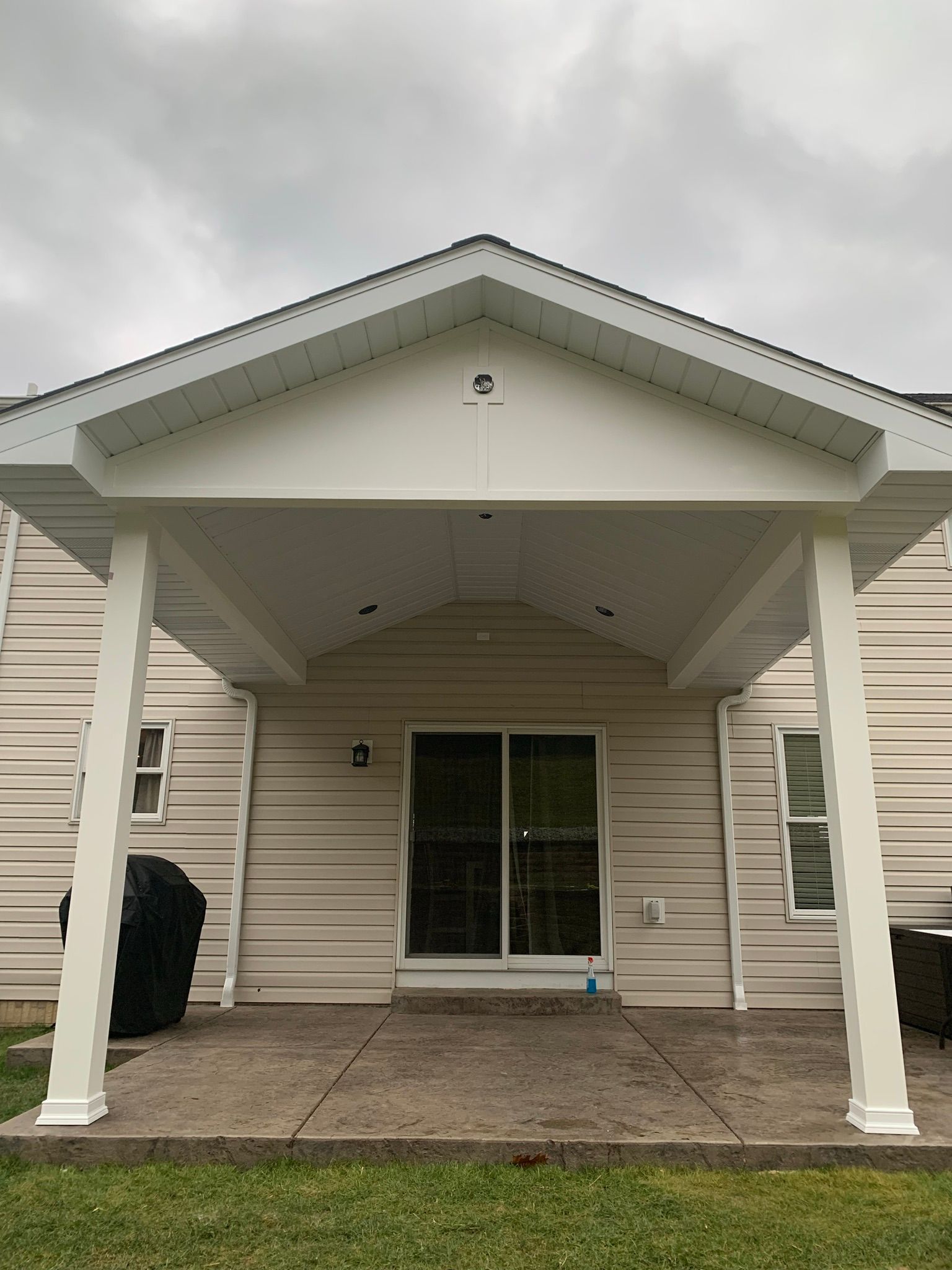 A covered patio with white pillars and siding; a sliding glass door and overcast sky are visible.