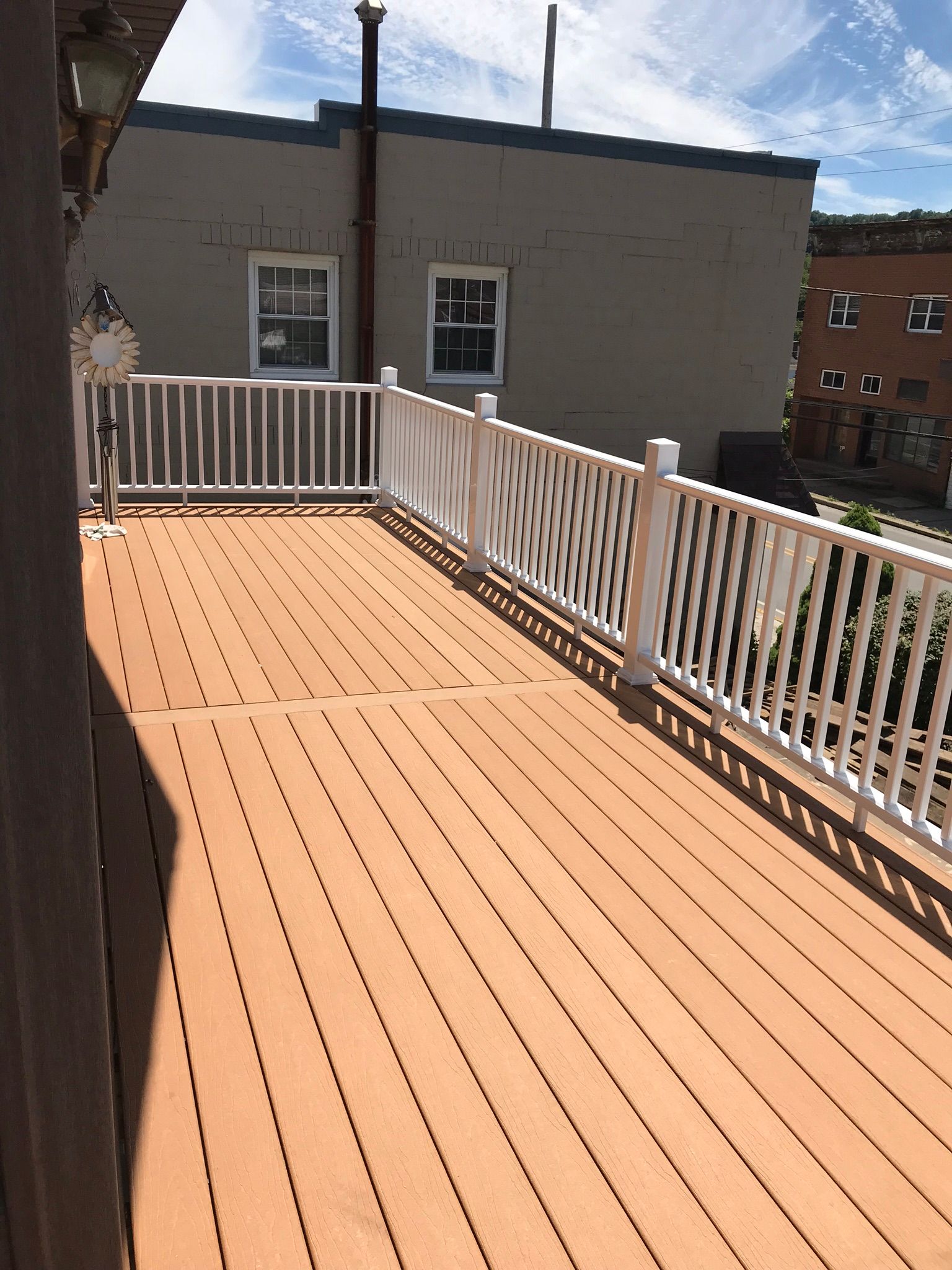 Wooden deck with white railing, overlooking a cityscape. Sunny day.