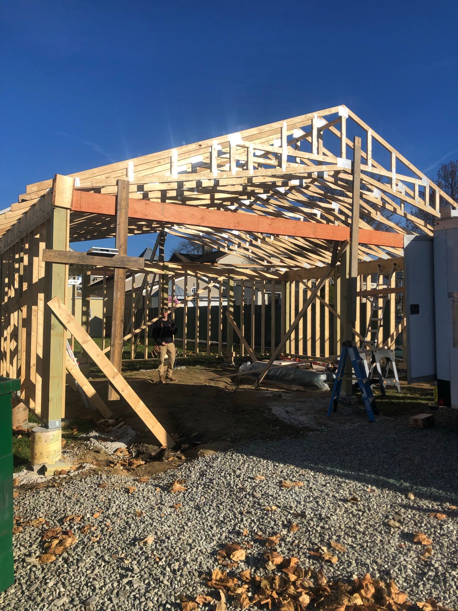 Construction of a wooden garage frame under a bright blue sky, with gravel ground.