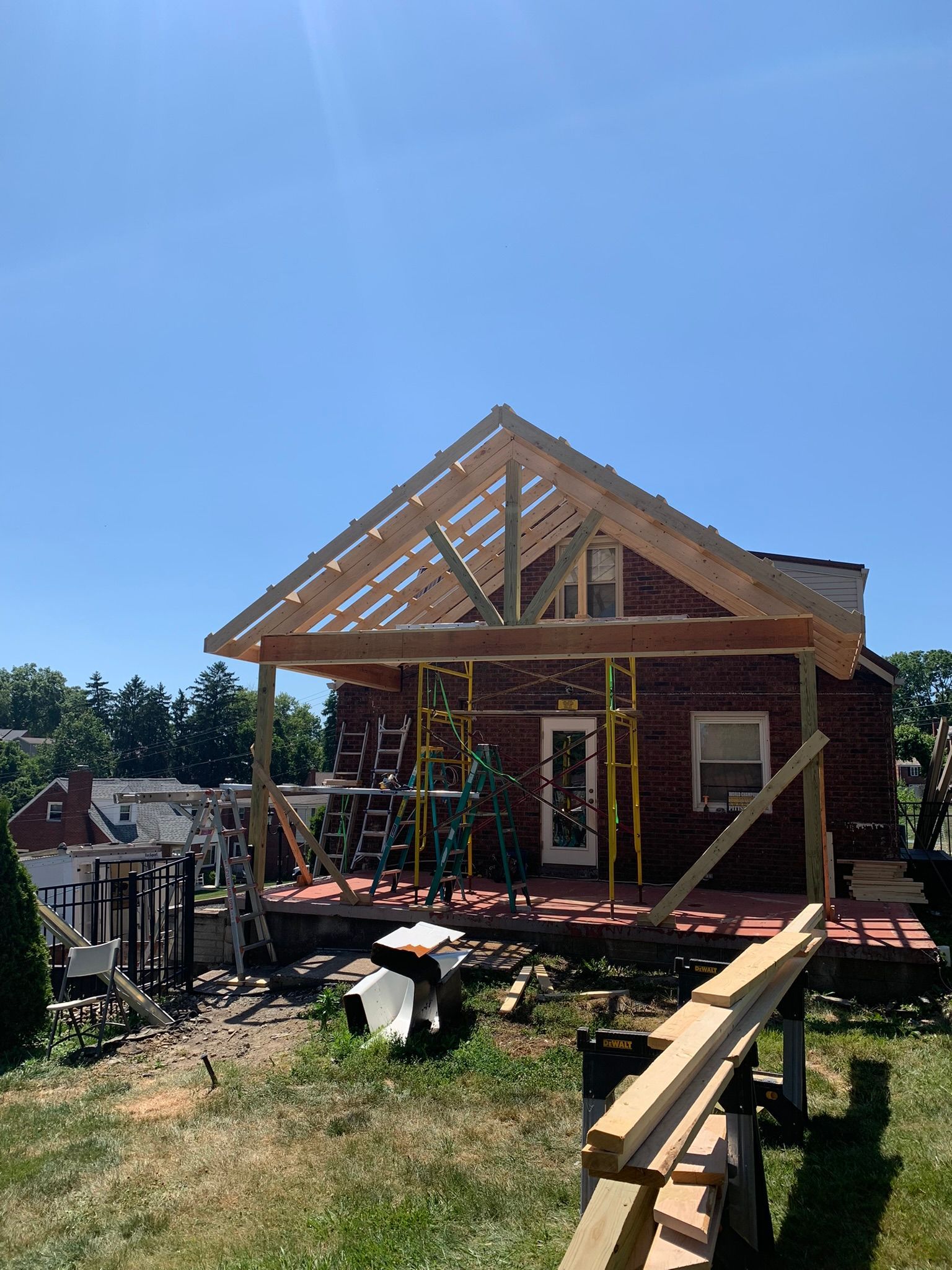 Construction of a wooden porch roof on a brick house; clear blue sky.