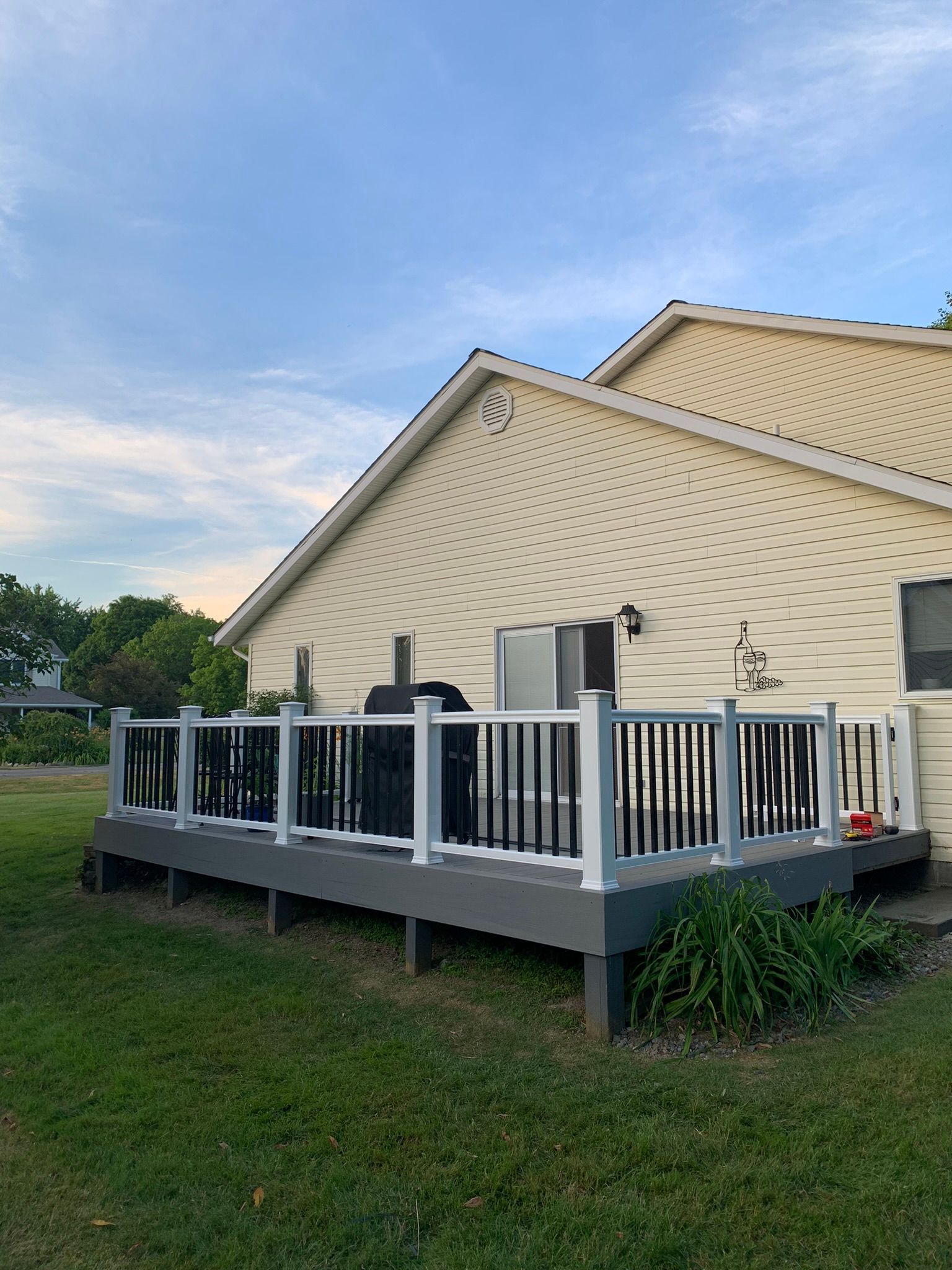 Gray and white deck attached to a yellow house, with a grill, in a grassy yard.