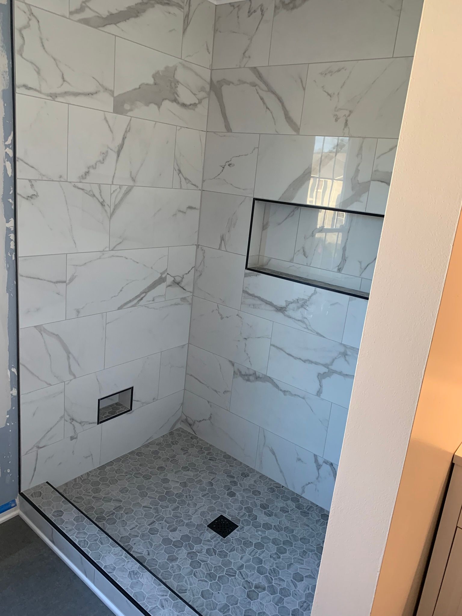 Tiled shower with marble-look walls, gray floor, and a built-in shelf.