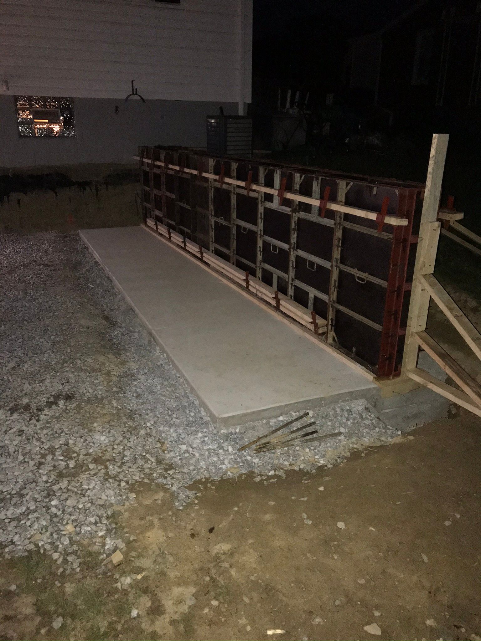 Concrete formwork with poured walkway, gravel base, and building in the background at night.