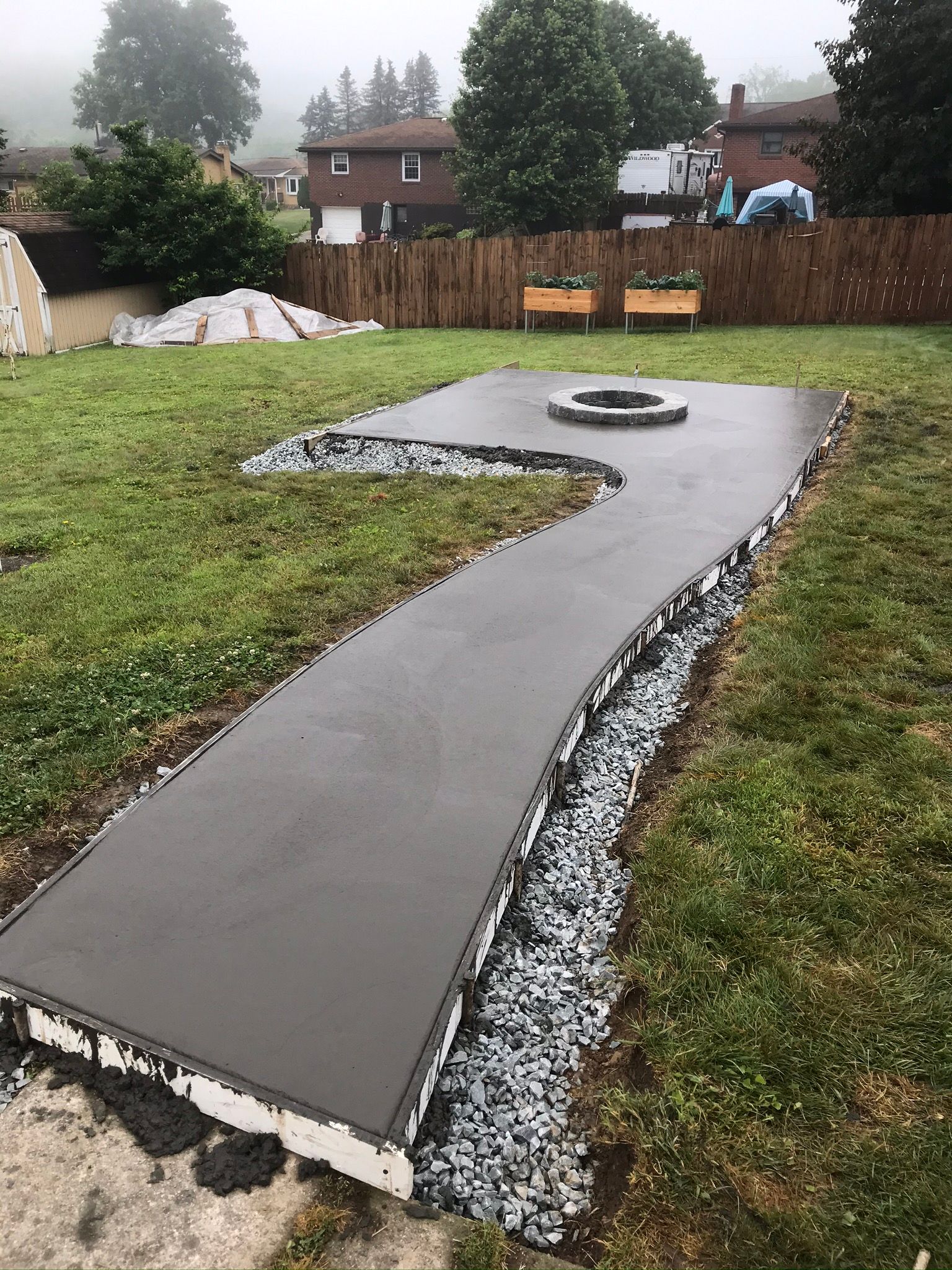 Newly poured concrete patio with a fire pit, bordered by gravel and grass.