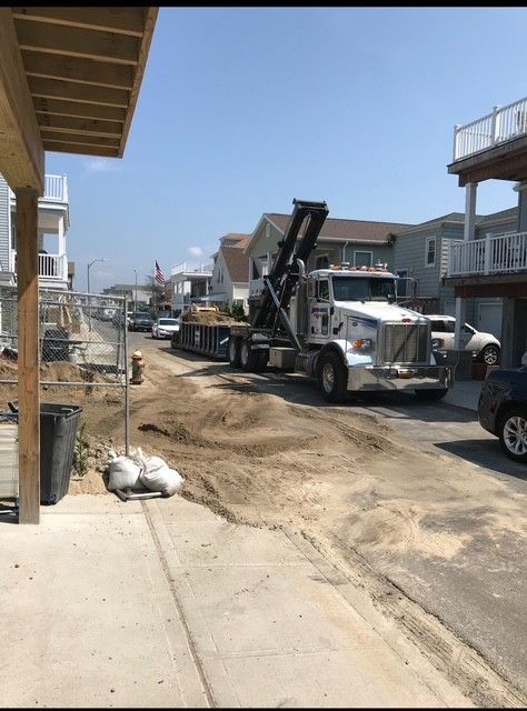 Truck with raised bed in a sandy street, houses in the background. Sunny day.