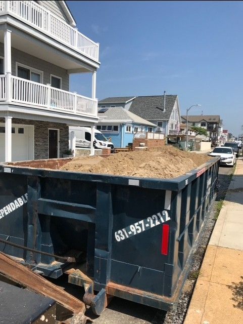 Dark blue dumpster filled with sand sits on a street in front of beach houses.