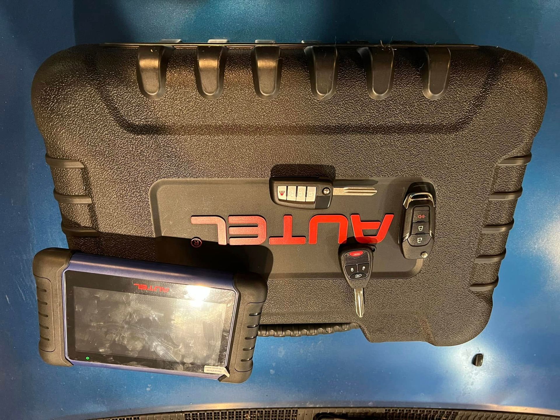 Black rugged AUTEL case with a handheld device and accessories on a blue background.