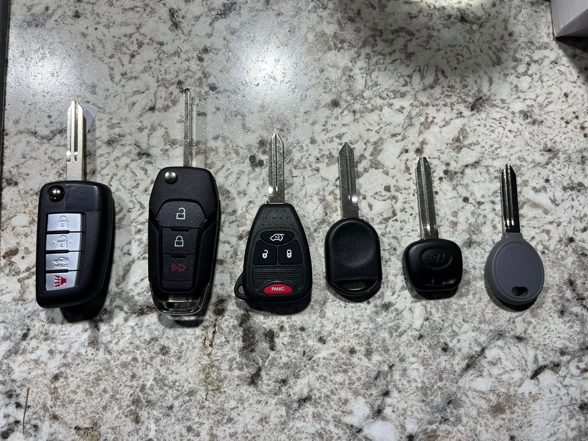 Six car key fobs and key blades arranged in a row on a speckled countertop.