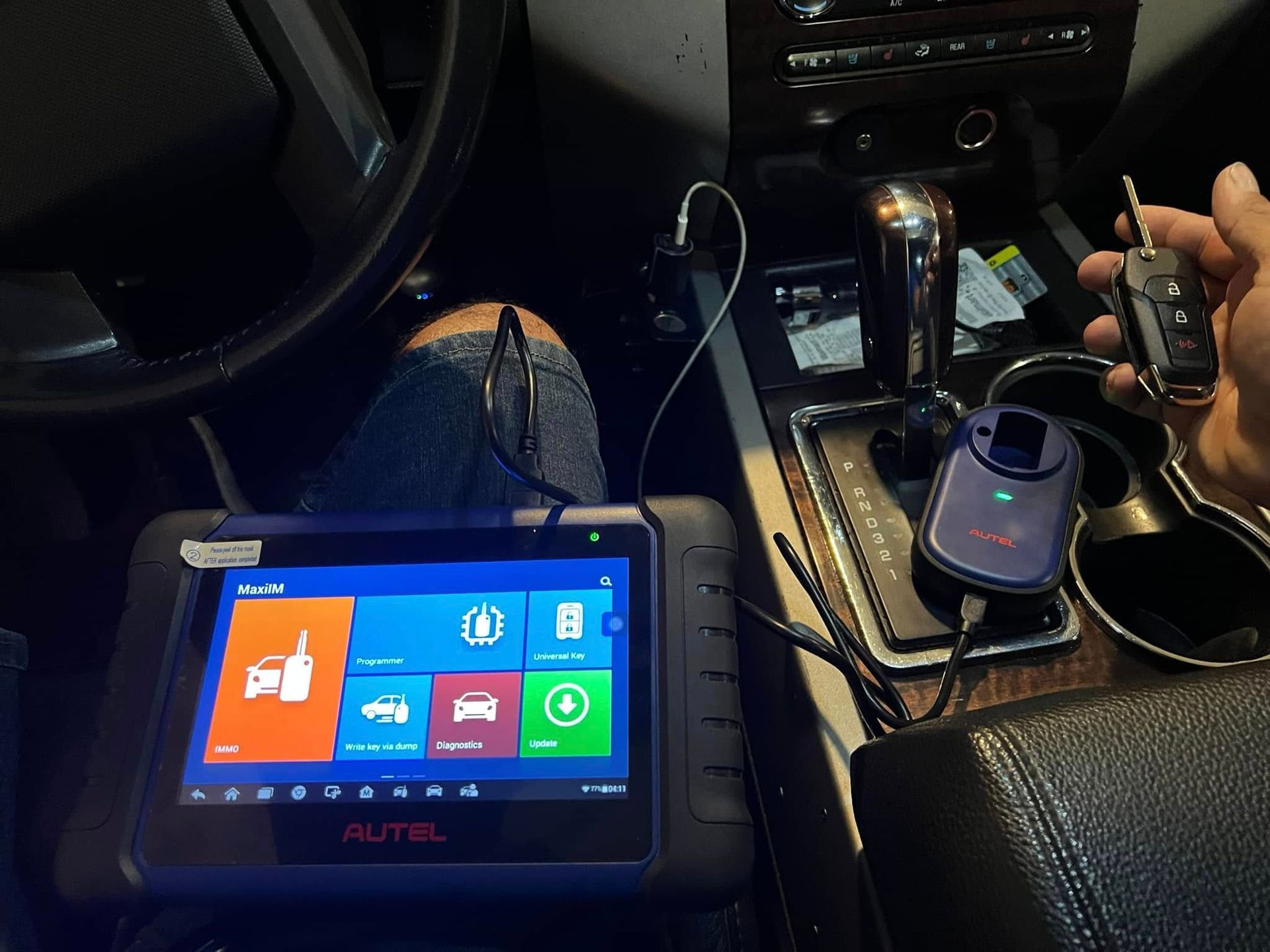 Car interior with a vehicle diagnostic tablet on the center console and a person holding a tool near the gear shifter