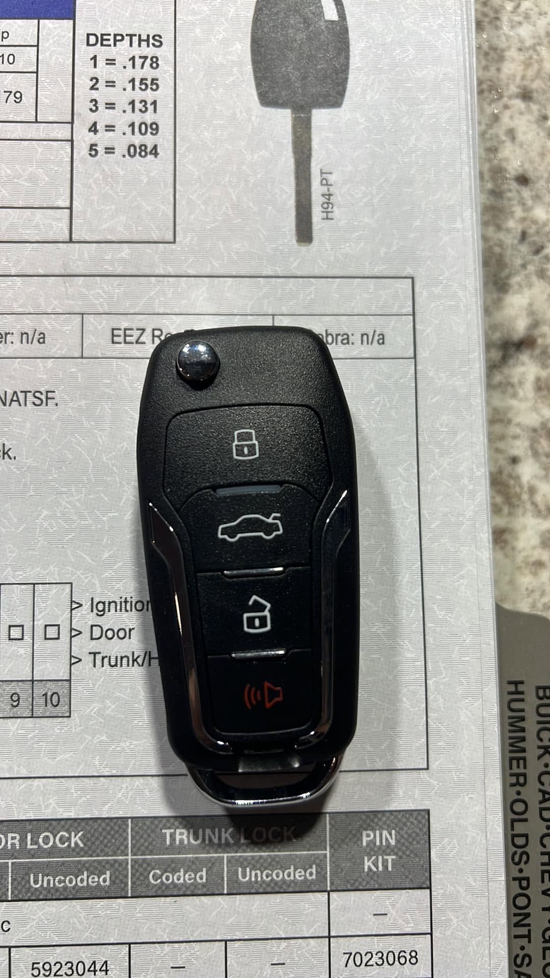 Black car key fob with lock, unlock, and trunk buttons on a printed document background