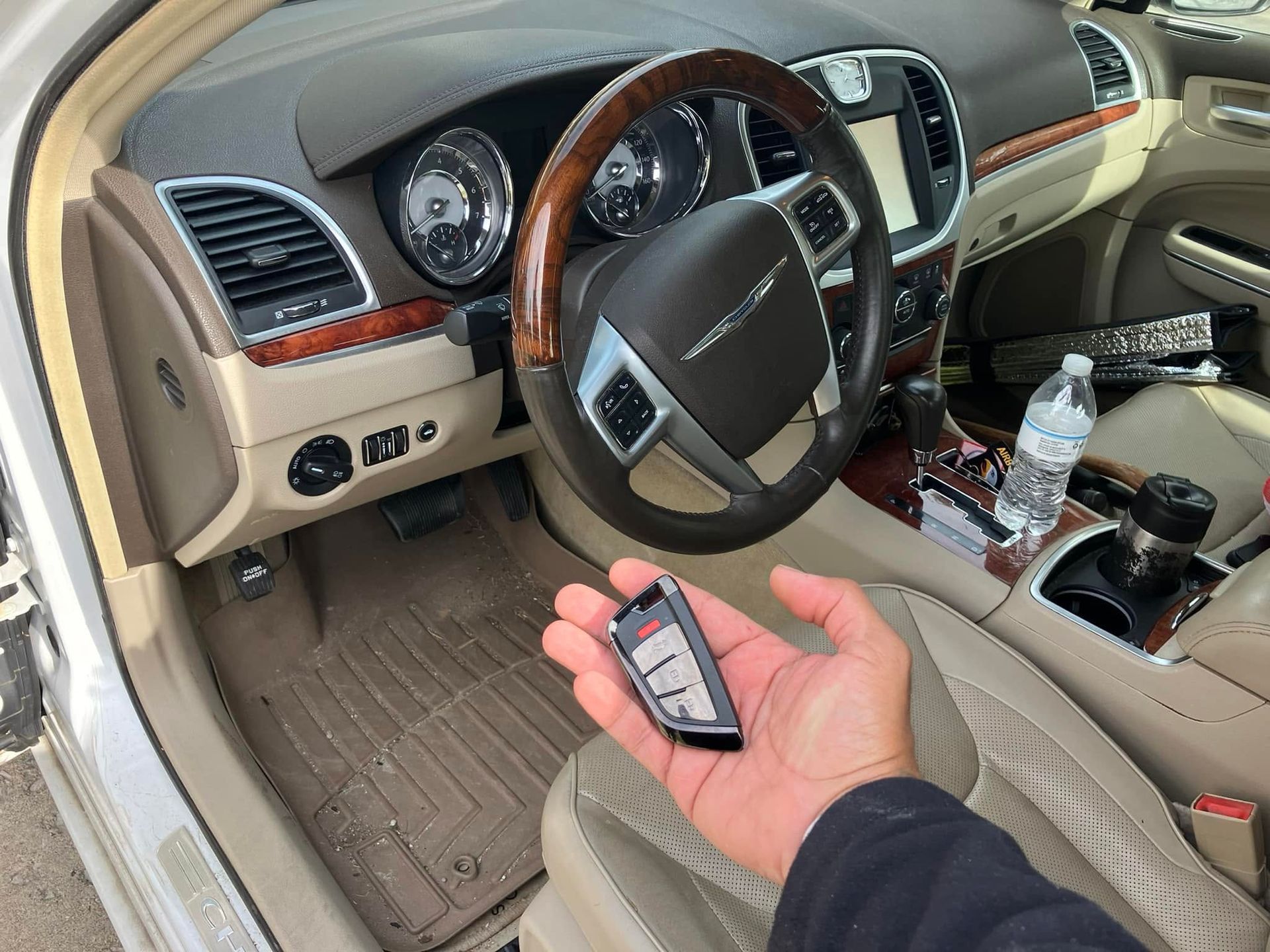 Hand holding a car key fob inside a beige car interior with steering wheel and center console visible