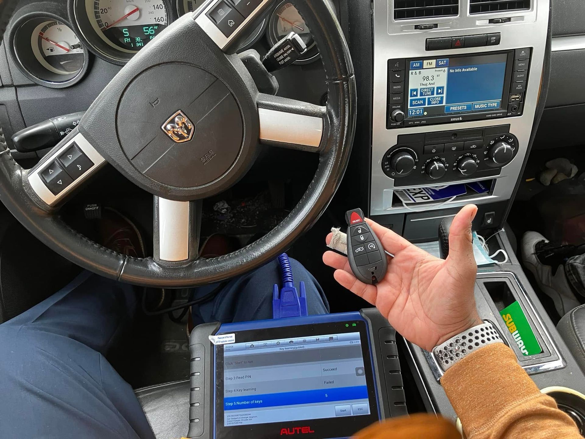 Car interior with driver holding a key fob beside a laptop and dashboard controls