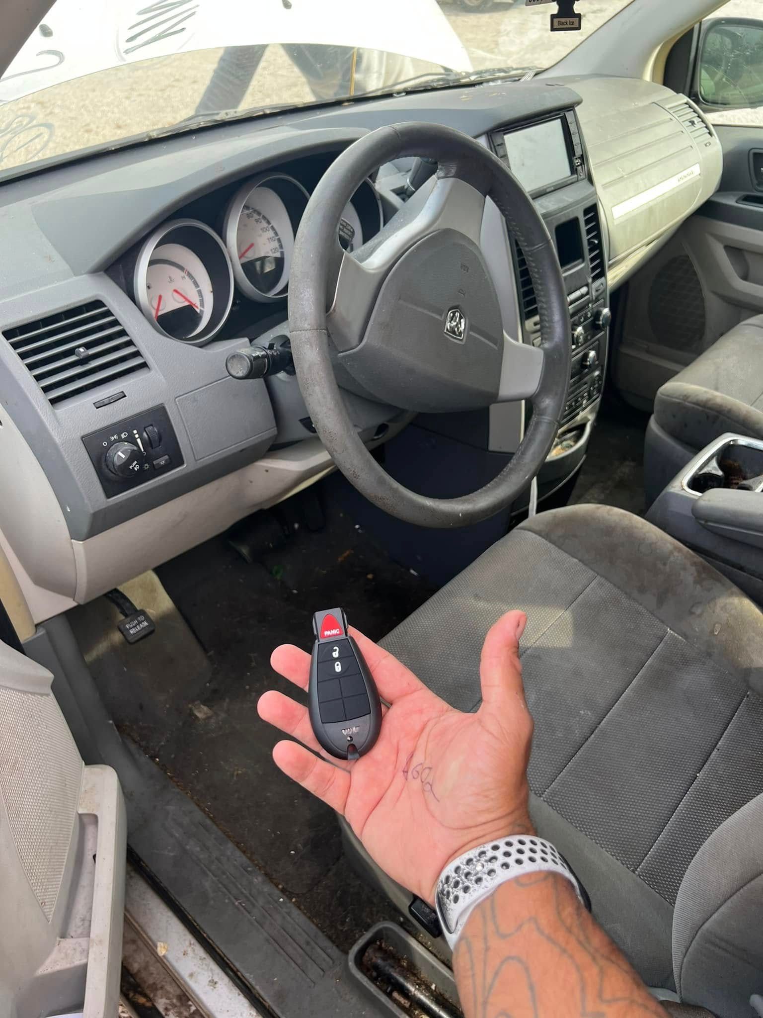 Car interior with a hand holding a car key fob near the driver's seat and steering wheel.