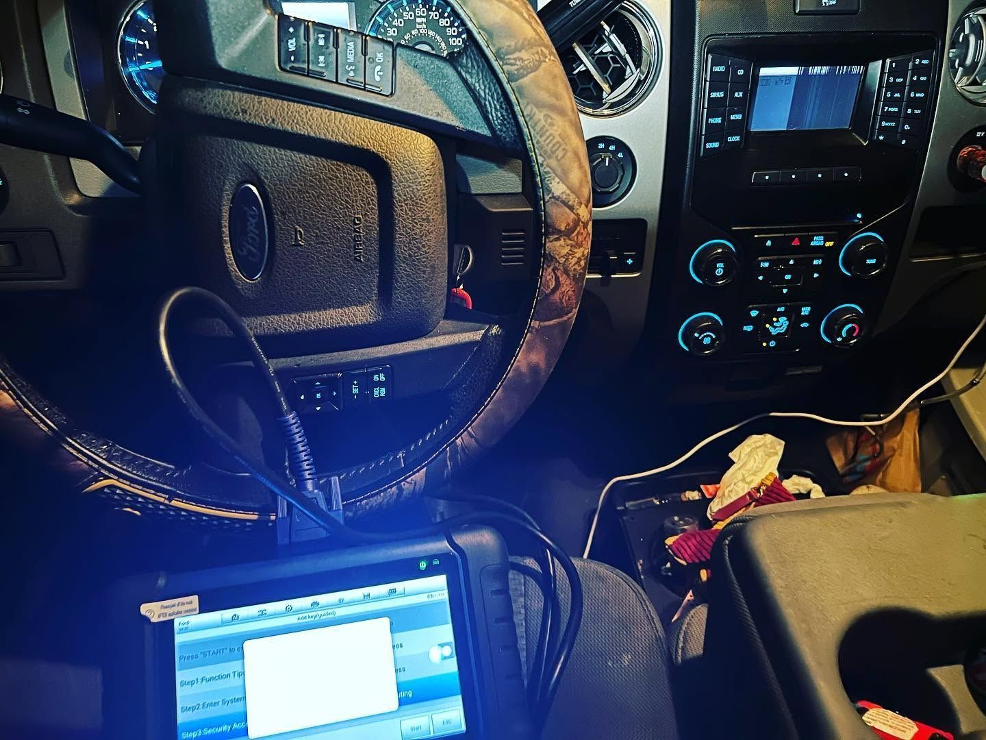 Car interior at night with illuminated dashboard, steering wheel, and a laptop on the passenger seat.