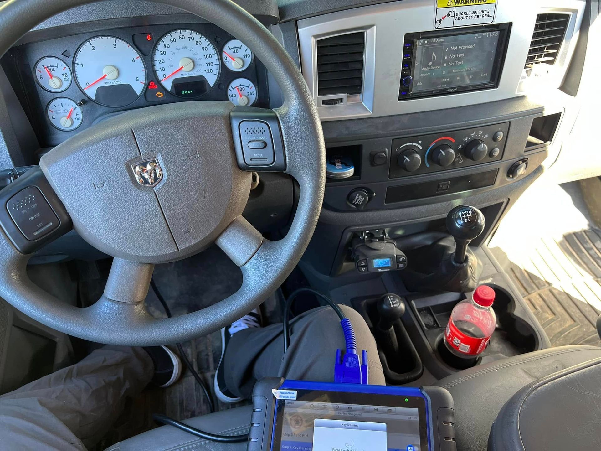 Truck cab interior with steering wheel, dashboard gauges, radio display, and drink bottles in the center console