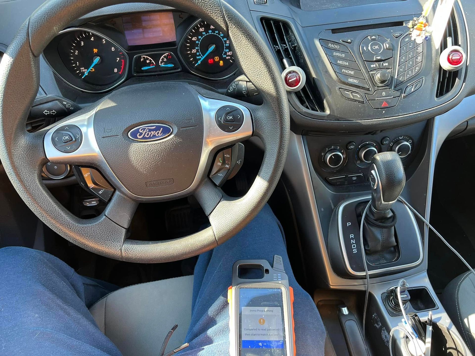 Car interior with Ford steering wheel, manual gear shift, dashboard, and a smartphone in the center console