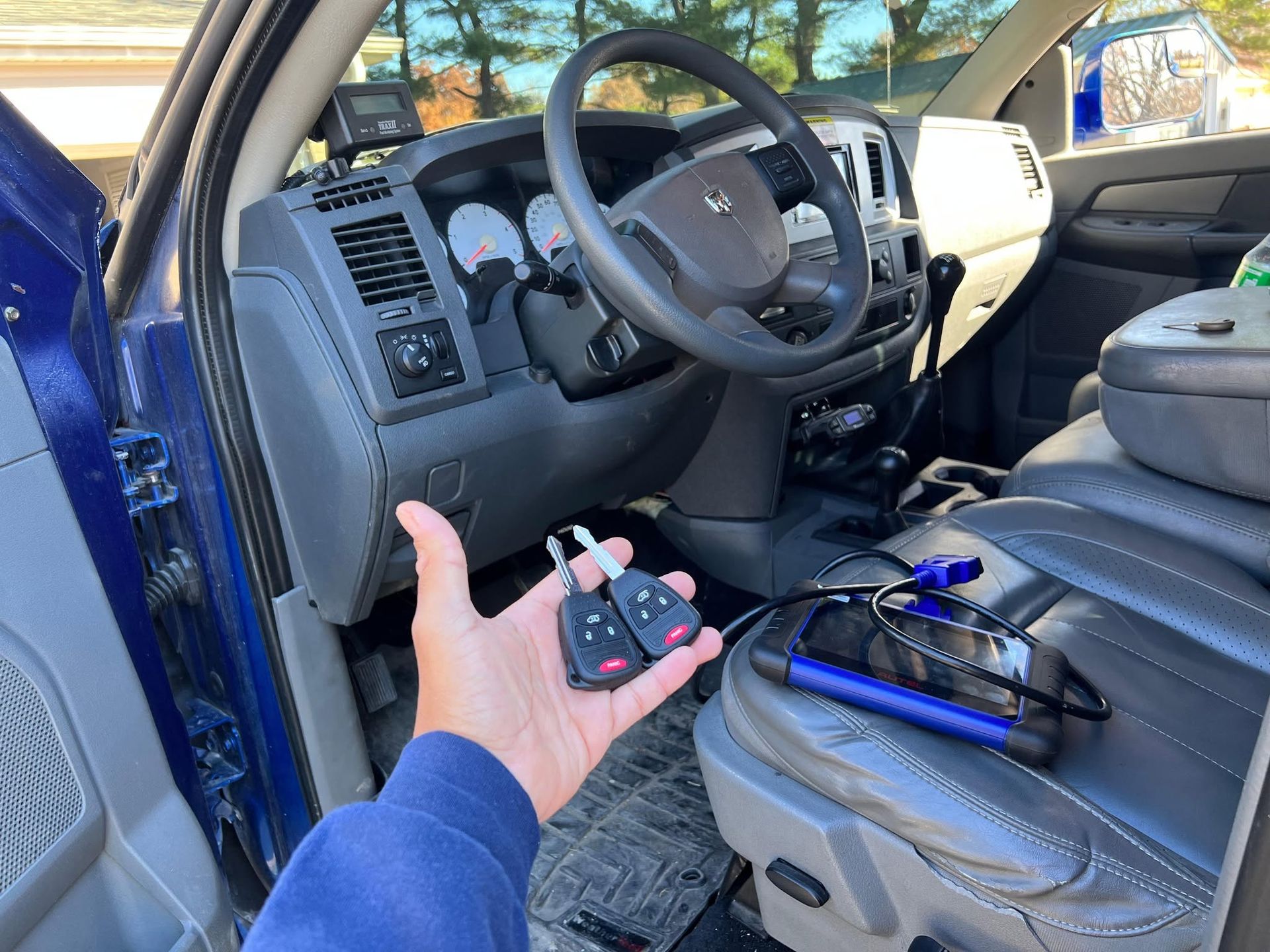 Hand holding a small electronic module inside a blue car’s driver seat area with tools nearby