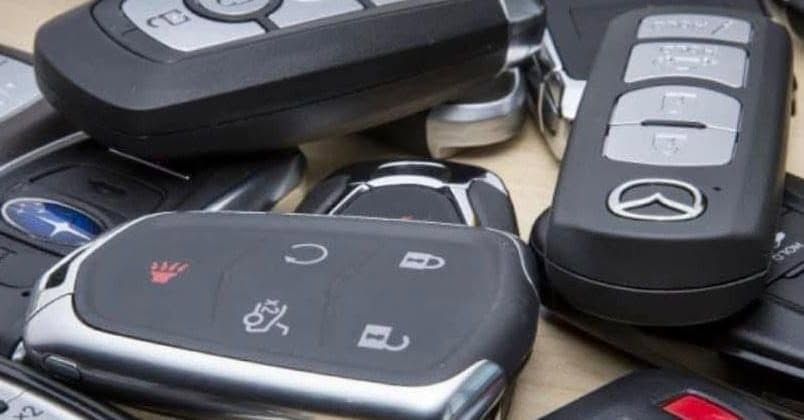 Assorted black car key fobs with buttons and logos, piled together on a surface
