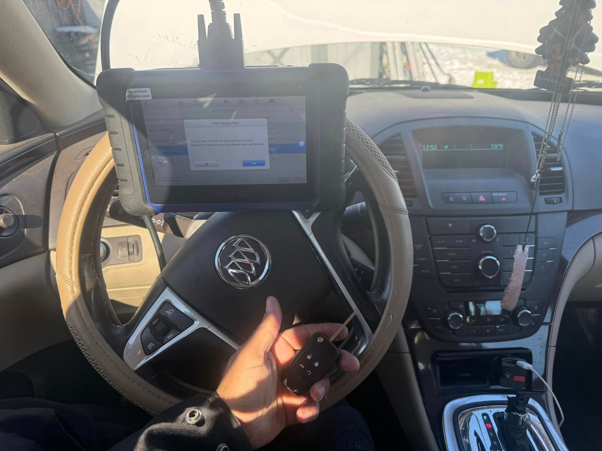 Driver’s seat view of a car interior with a steering wheel, tablet mount, center console, and a hand holding a key fob.