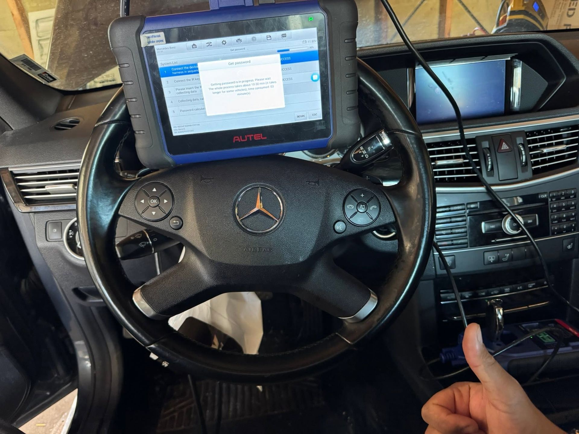 Mercedes car dashboard with steering wheel and mounted tablet navigation screen; hand pointing at center console
