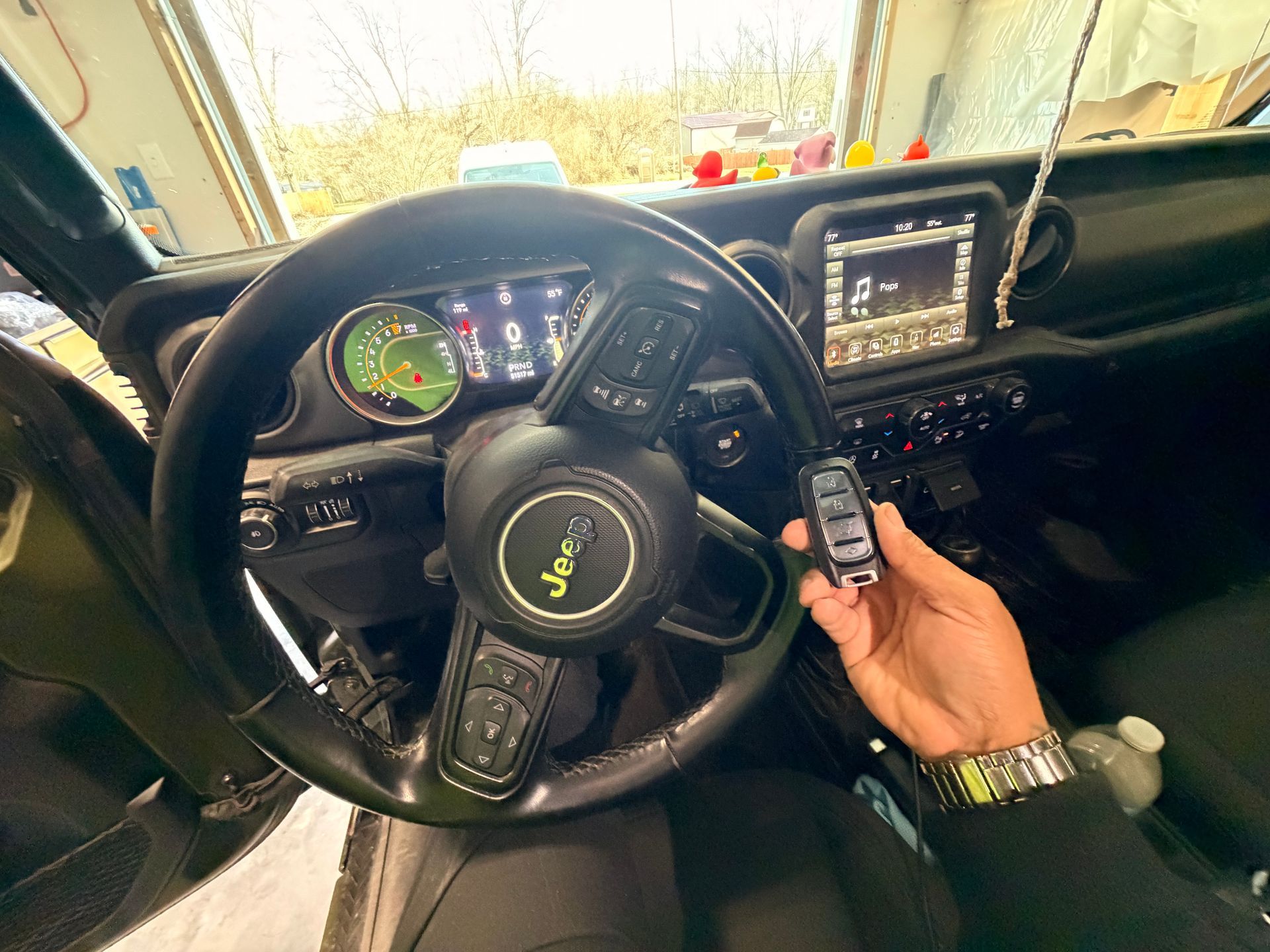 Inside a Jeep, driver holds a key fob near the steering wheel and dashboard display