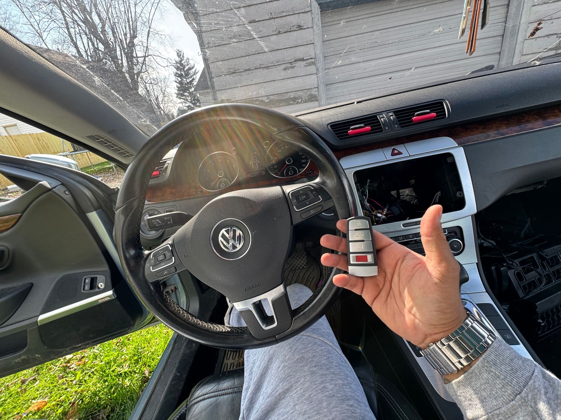 Hand holding a car key fob beside a steering wheel and dashboard in a parked car.