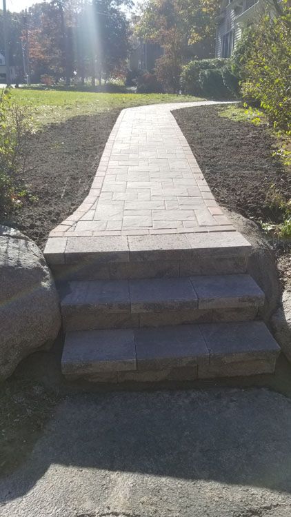 A stone walkway with stairs leading up to a grassy area 
