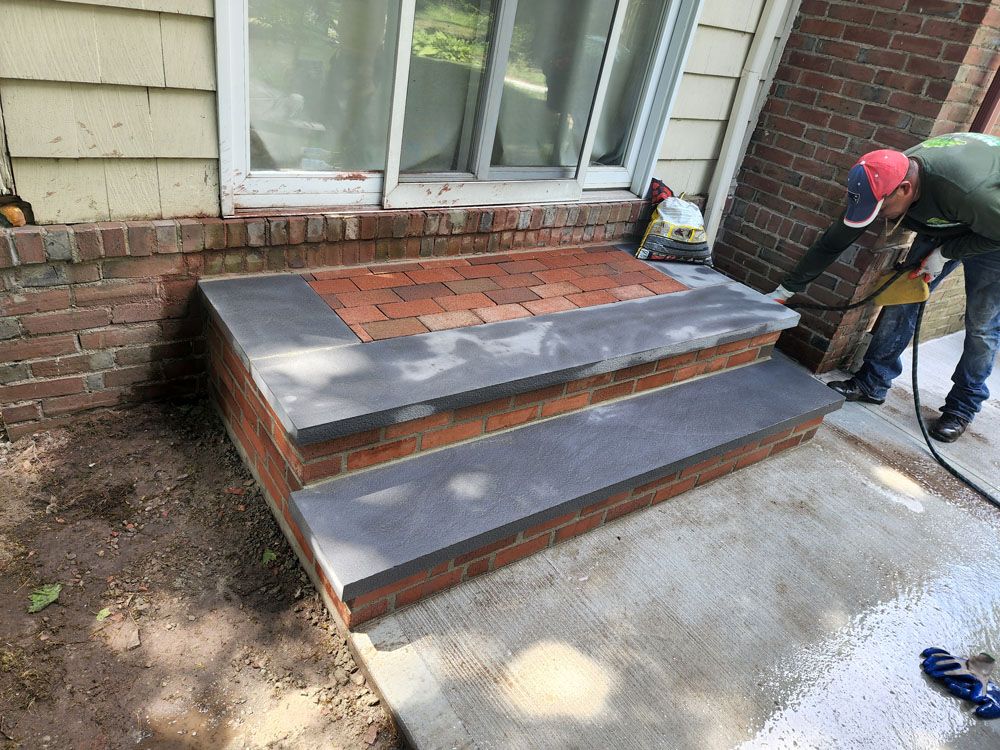A man is working on a set of stairs in front of a brick house